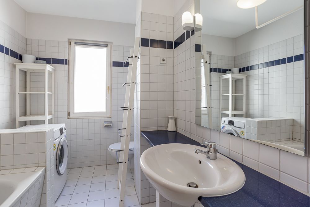 Helles Badezimmer mit Waschbecken, Spiegel, Waschmaschine und weißen Fliesen.
