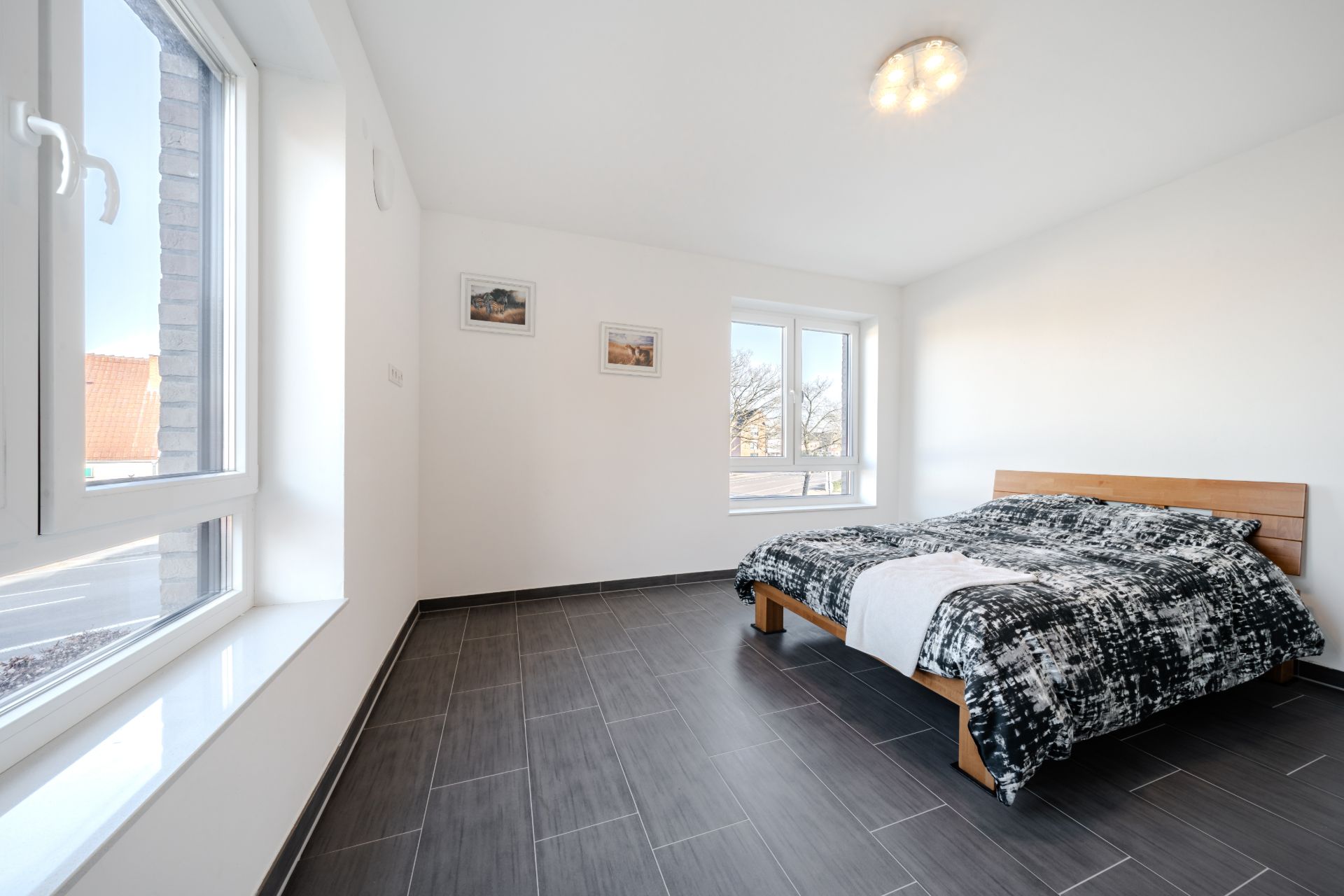 Helles Schlafzimmer mit großem Fenster, Doppelbett und Fliesenboden.
