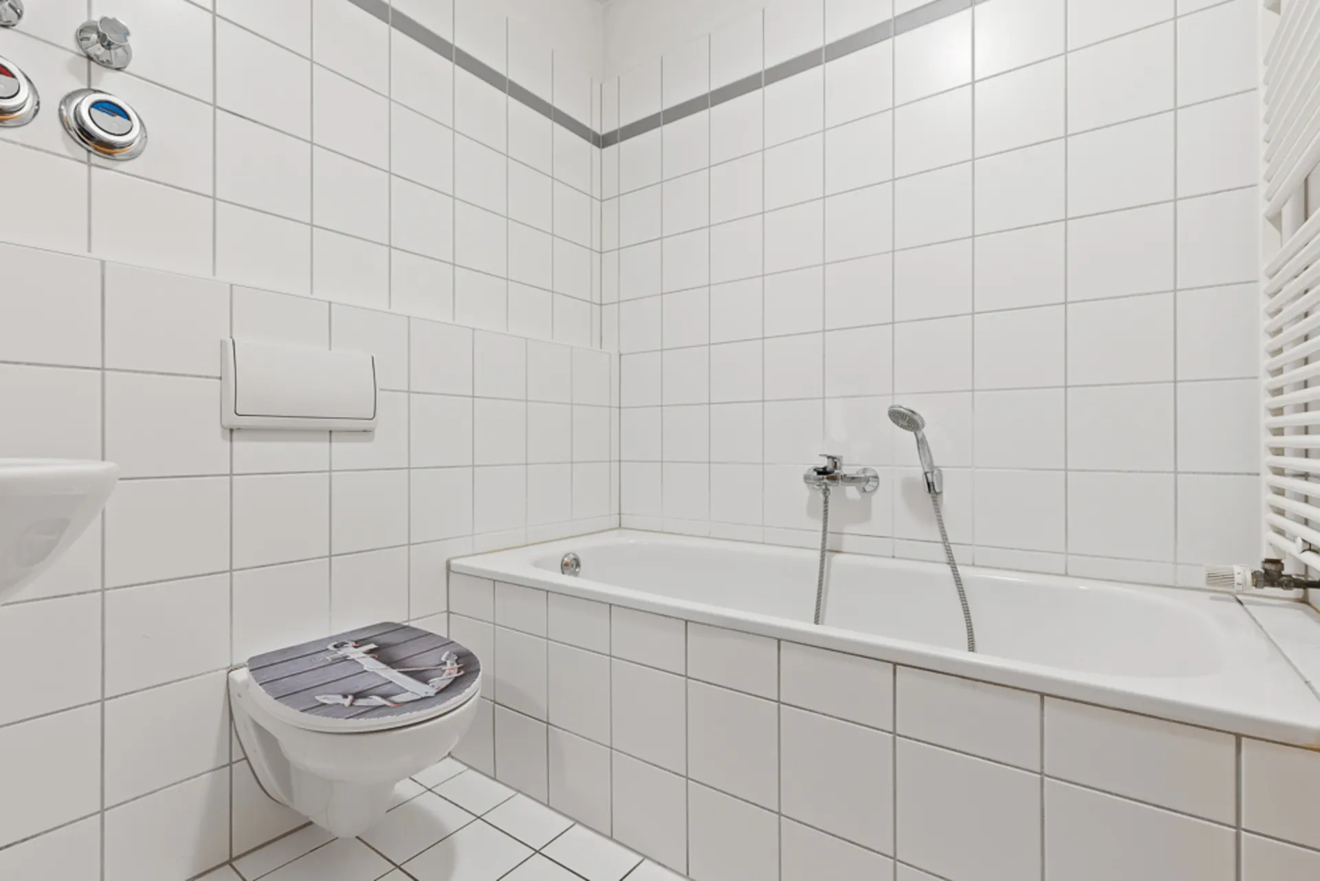 Modernes Bad mit weiß gefliester Badewanne, WC und Handbrause.