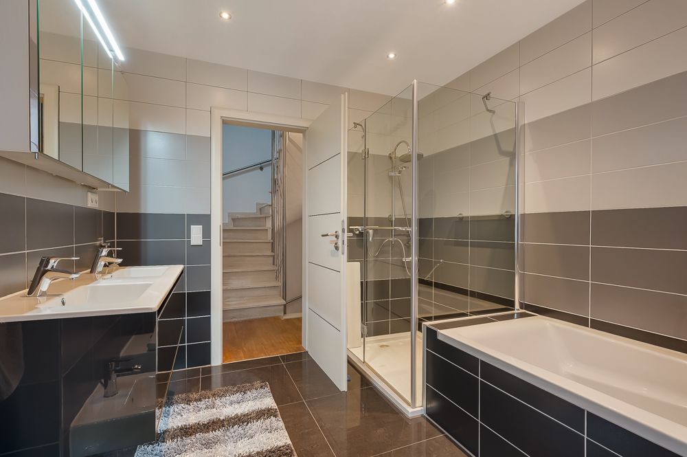Modernes Badezimmer mit Doppelwaschbecken, Dusche, Badewanne und Blick auf eine Treppe.