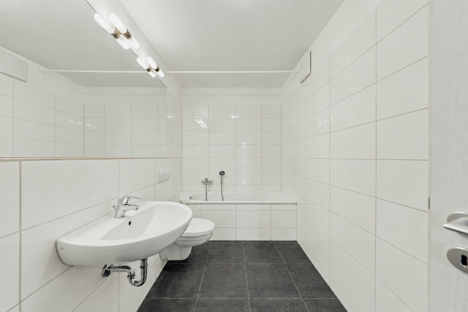 Modernes Badezimmer mit weiß gefliesten Wänden, Waschbecken, Toilette und Badewanne.
