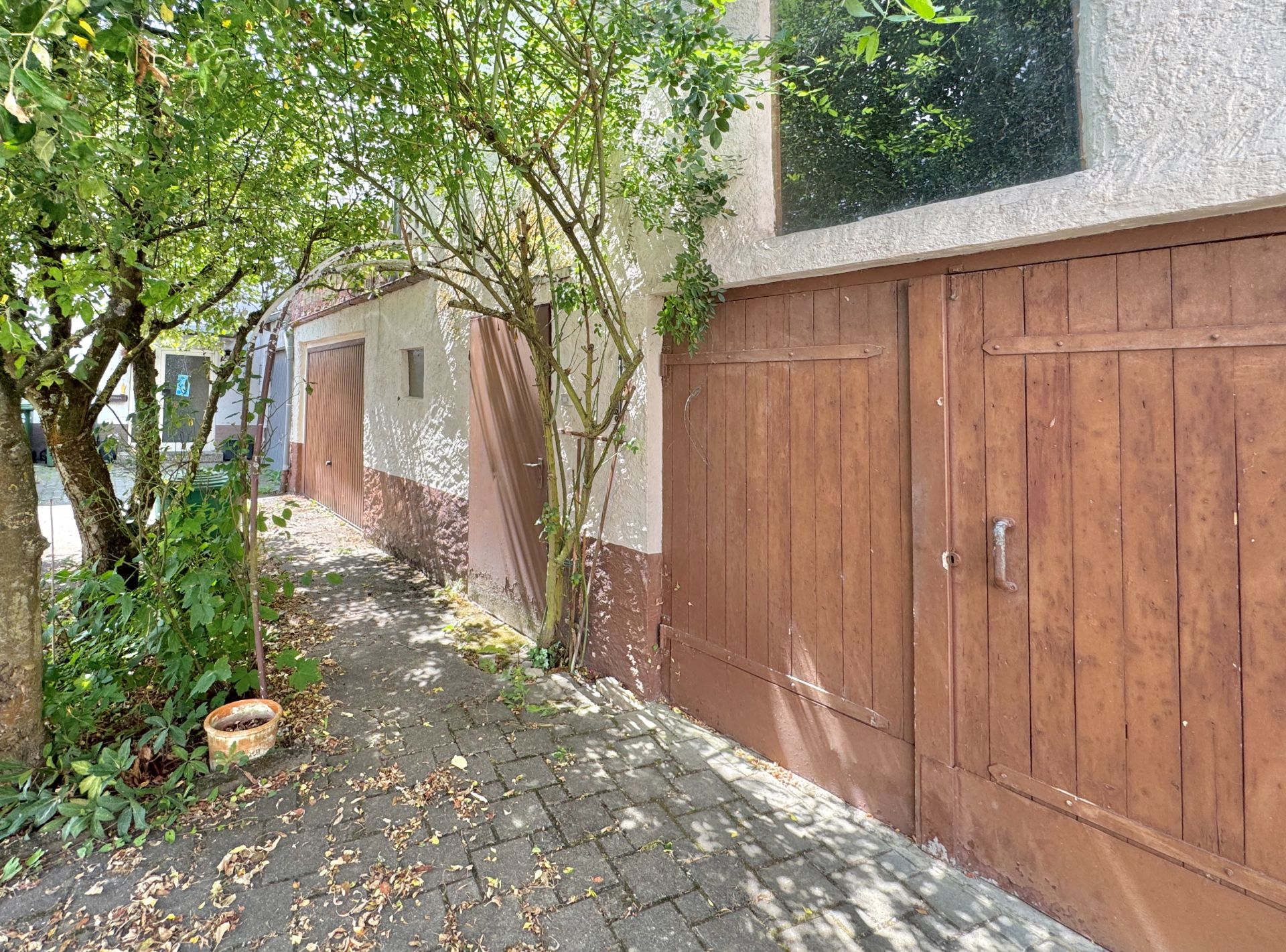 Außenansicht mit braunen Garagentoren, Bäumen und einem gepflasterten Weg.