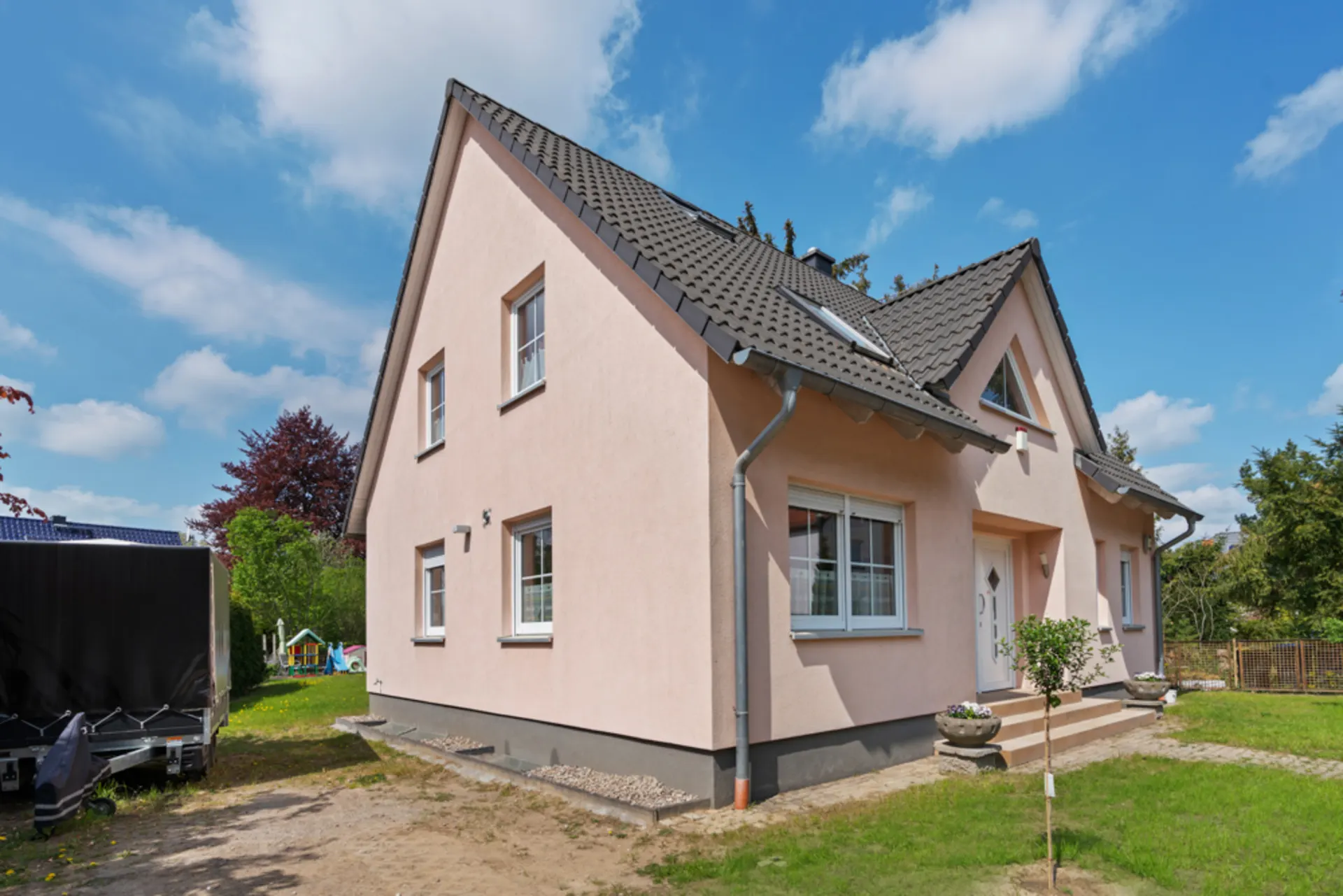 Zweistöckiges Einfamilienhaus mit rosa Fassade, Dachschrägen und Garten bei sonnigem Wetter.