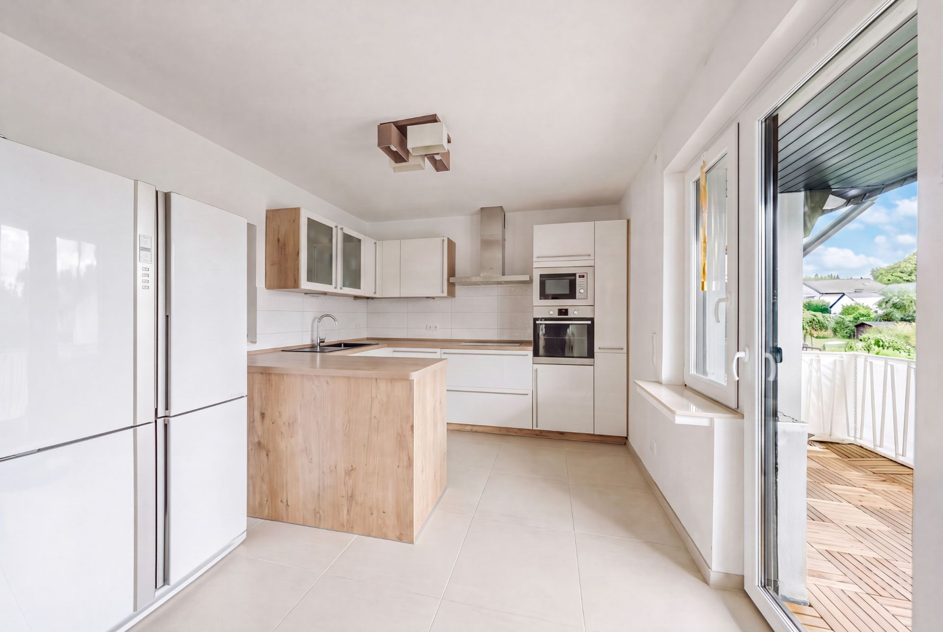Helle Wohnküche mit Kochinsel, weißen Schränken und Zugang zum Balkon.