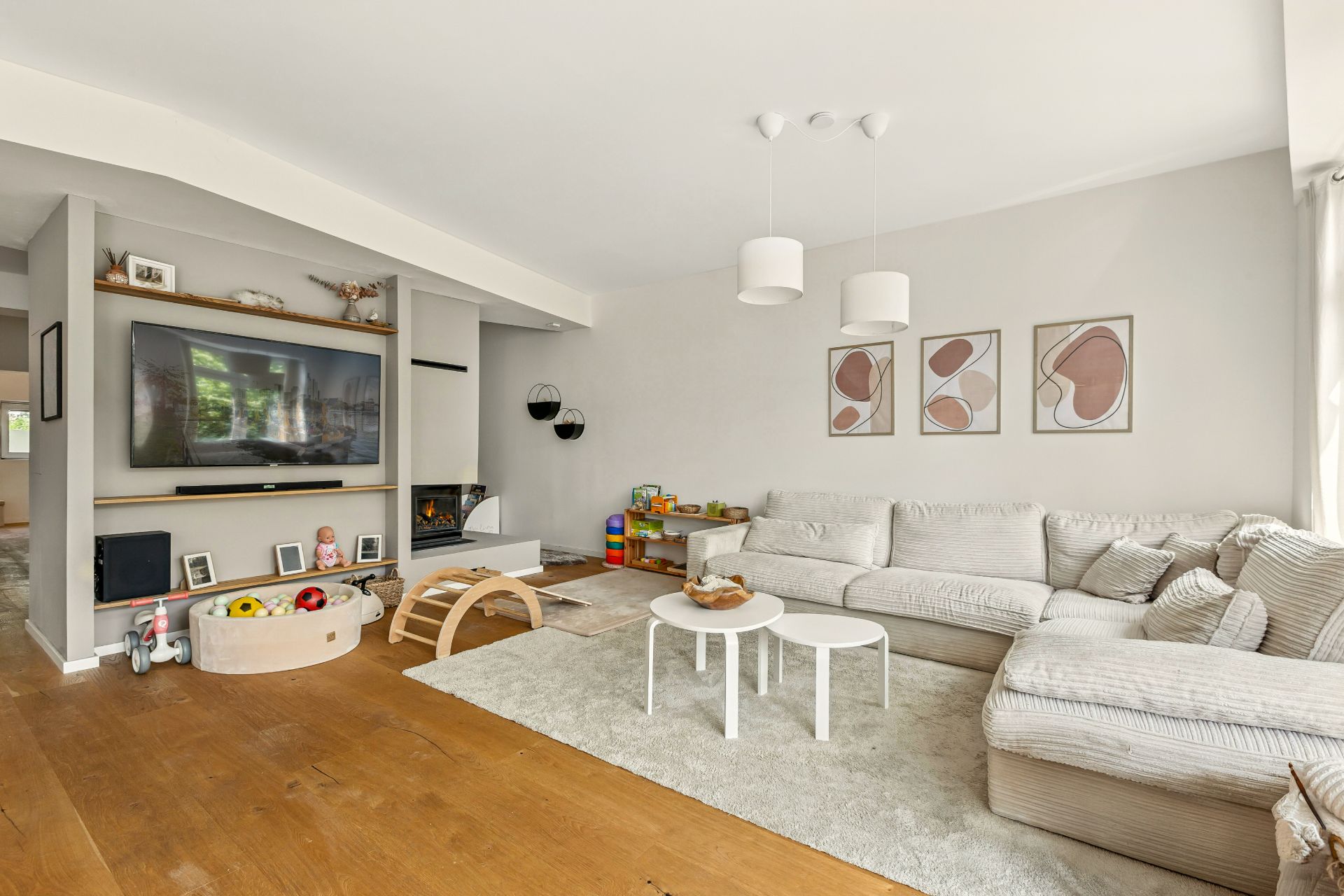 Helles Wohnzimmer mit Ecksofa, Couchtischen, Spielzeug und Fernseher an der Wand.