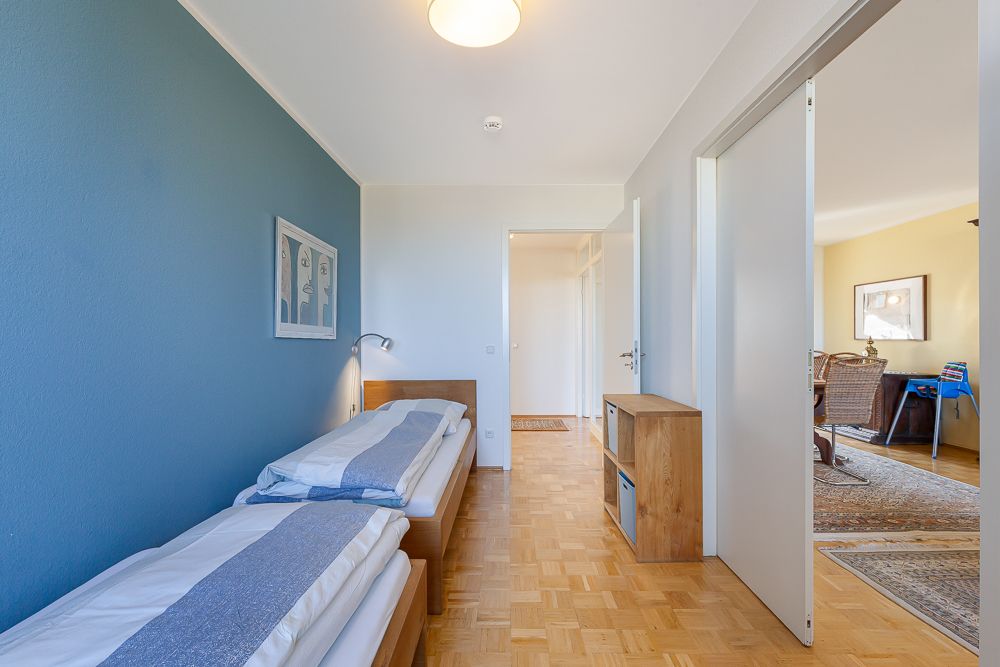 Schlafzimmer mit zwei Einzelbetten, Holzmöbeln und blau gestrichener Wand.