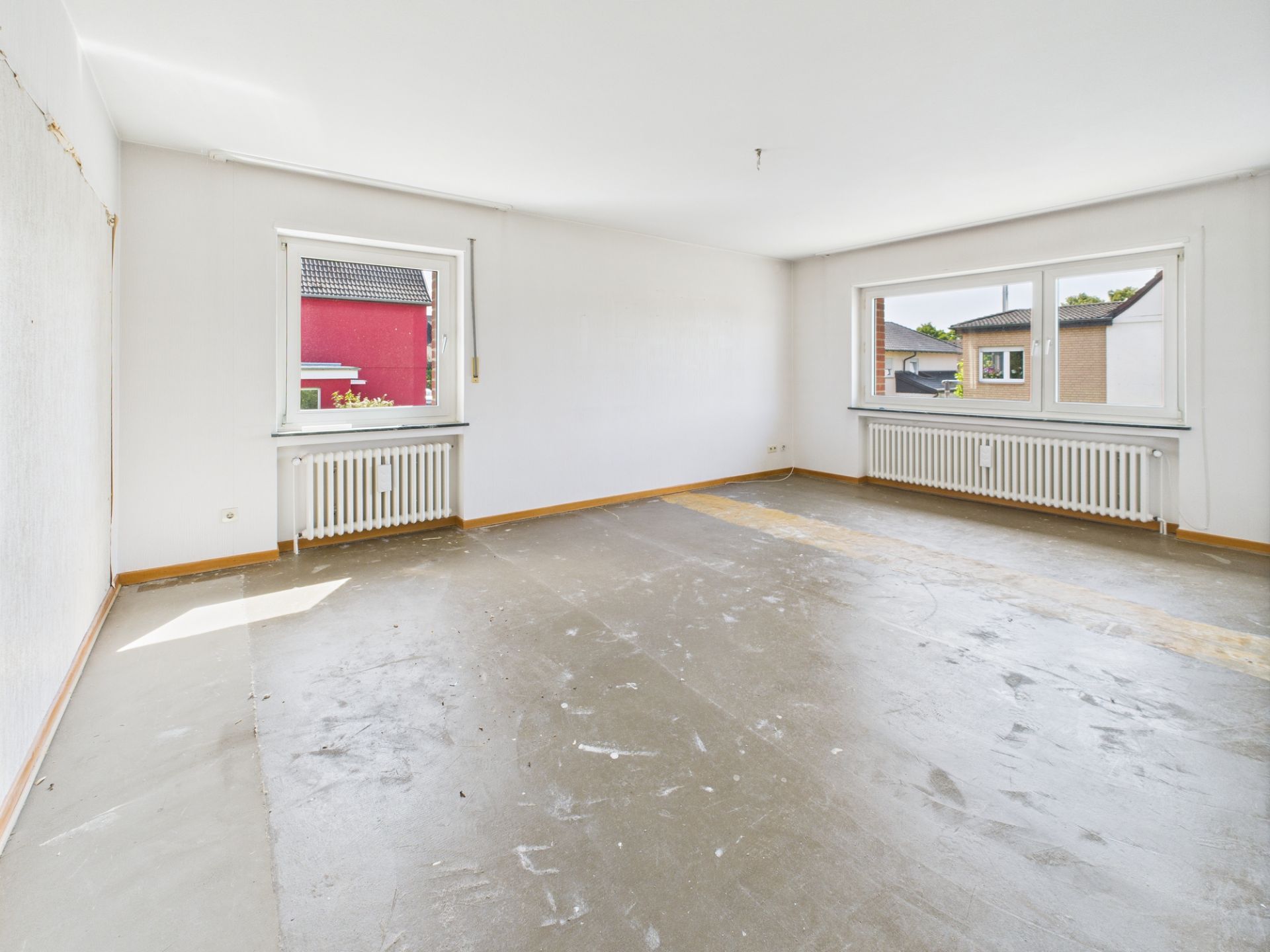 Leeres Zimmer mit zwei Heizkörpern und drei Fenstern, Boden ohne Belag.