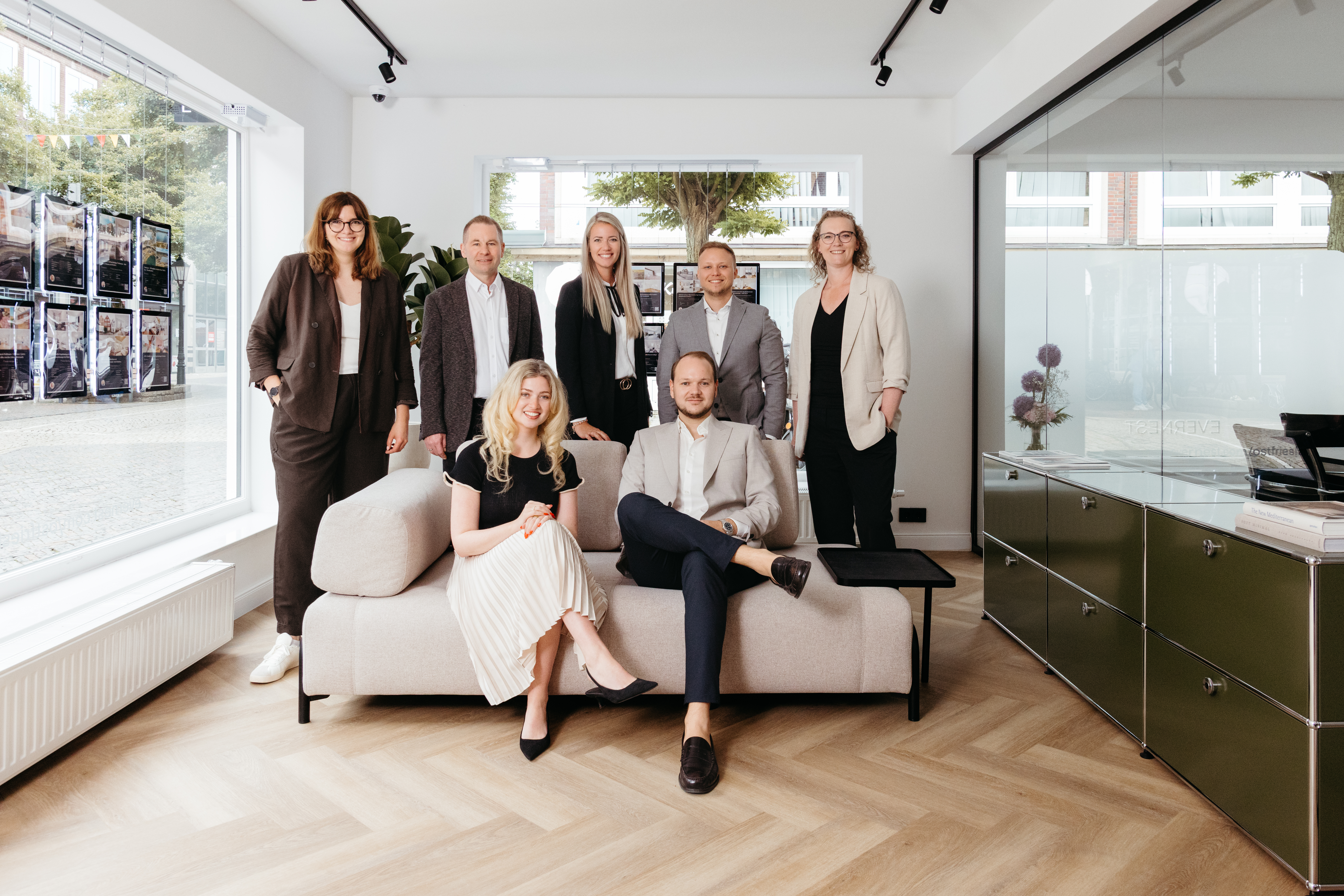 Fünf Personen in Businesskleidung stehen vor einem Gebäude mit Säulen.