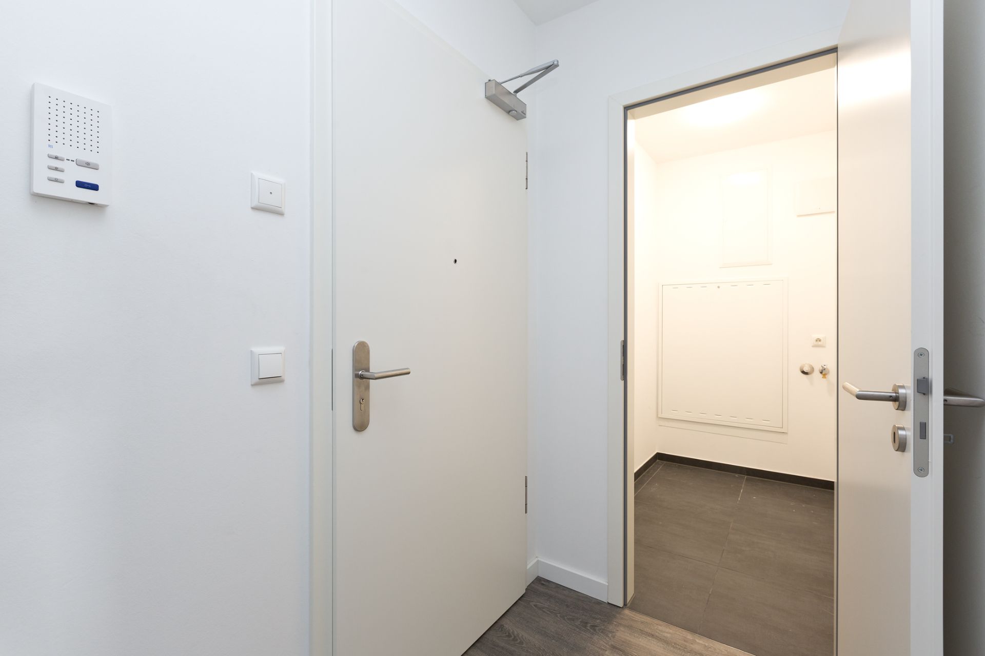 Heller Flur mit weißen Türen, dunklem Boden und Wandpanel.