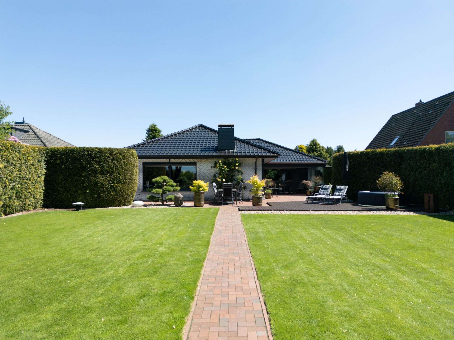 Einfamilienhaus mit Terrasse und gepflegtem Garten, umgeben von Hecken.