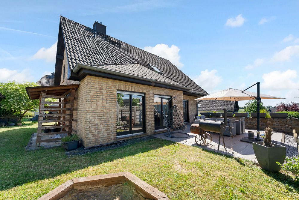 Backstein-Einfamilienhaus mit Terrasse, Grill und Sitzbereich im Garten bei sonnigem Wetter.