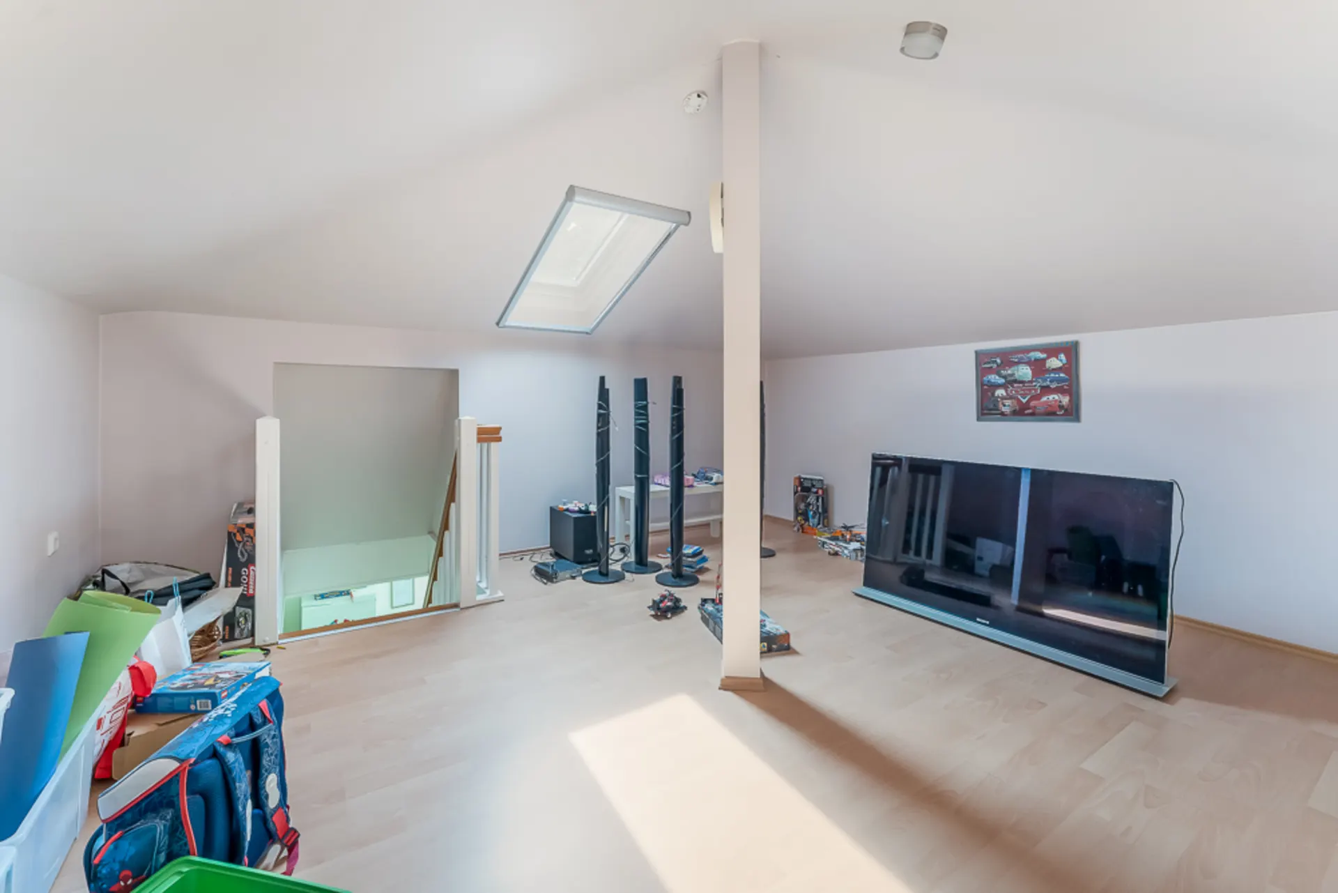 Dachzimmer mit schräger Decke, Oberlicht, Fernseher, Spielsachen und Kisten auf dem Boden.