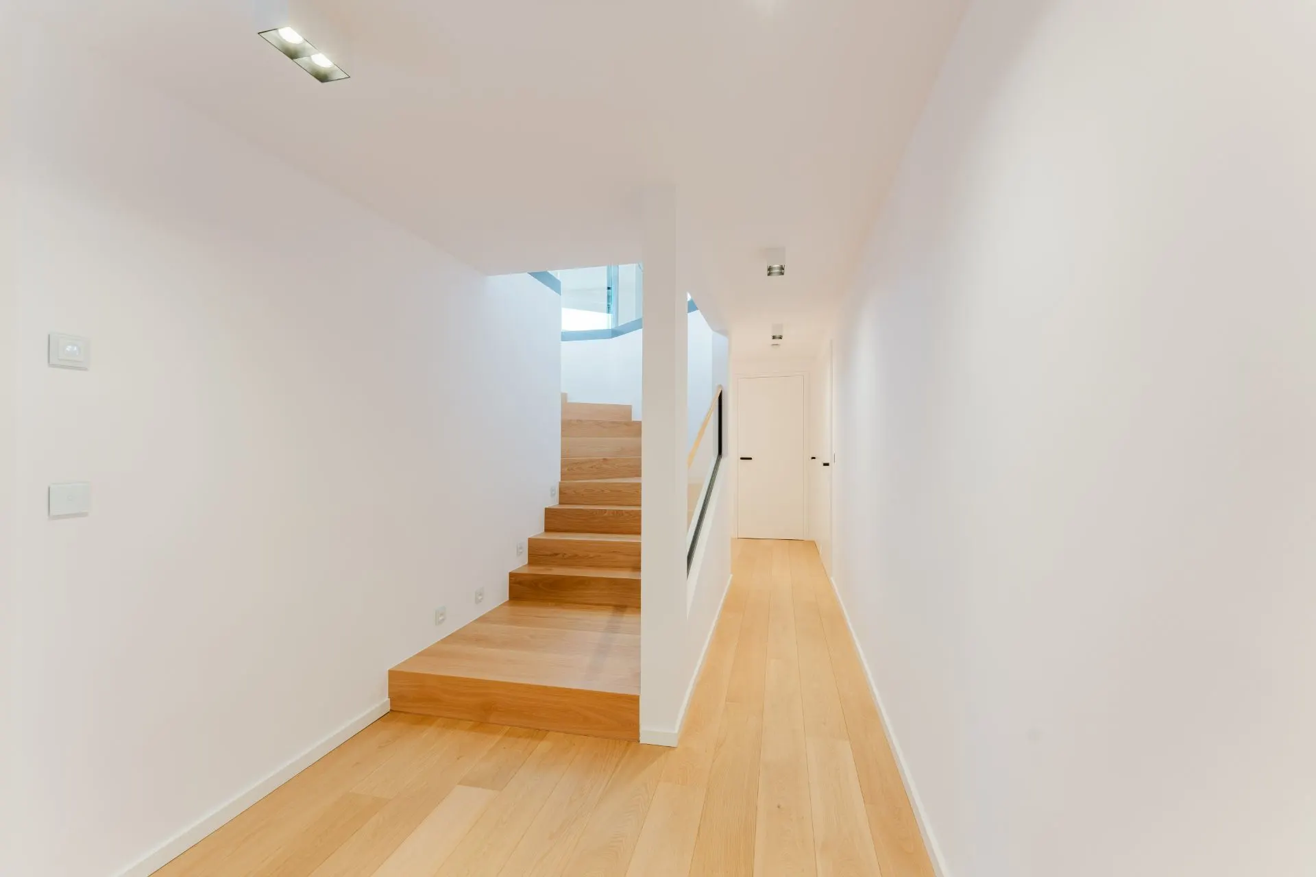 Heller Flur mit Holztreppe und Türen, weißen Wänden und Holzfußboden.