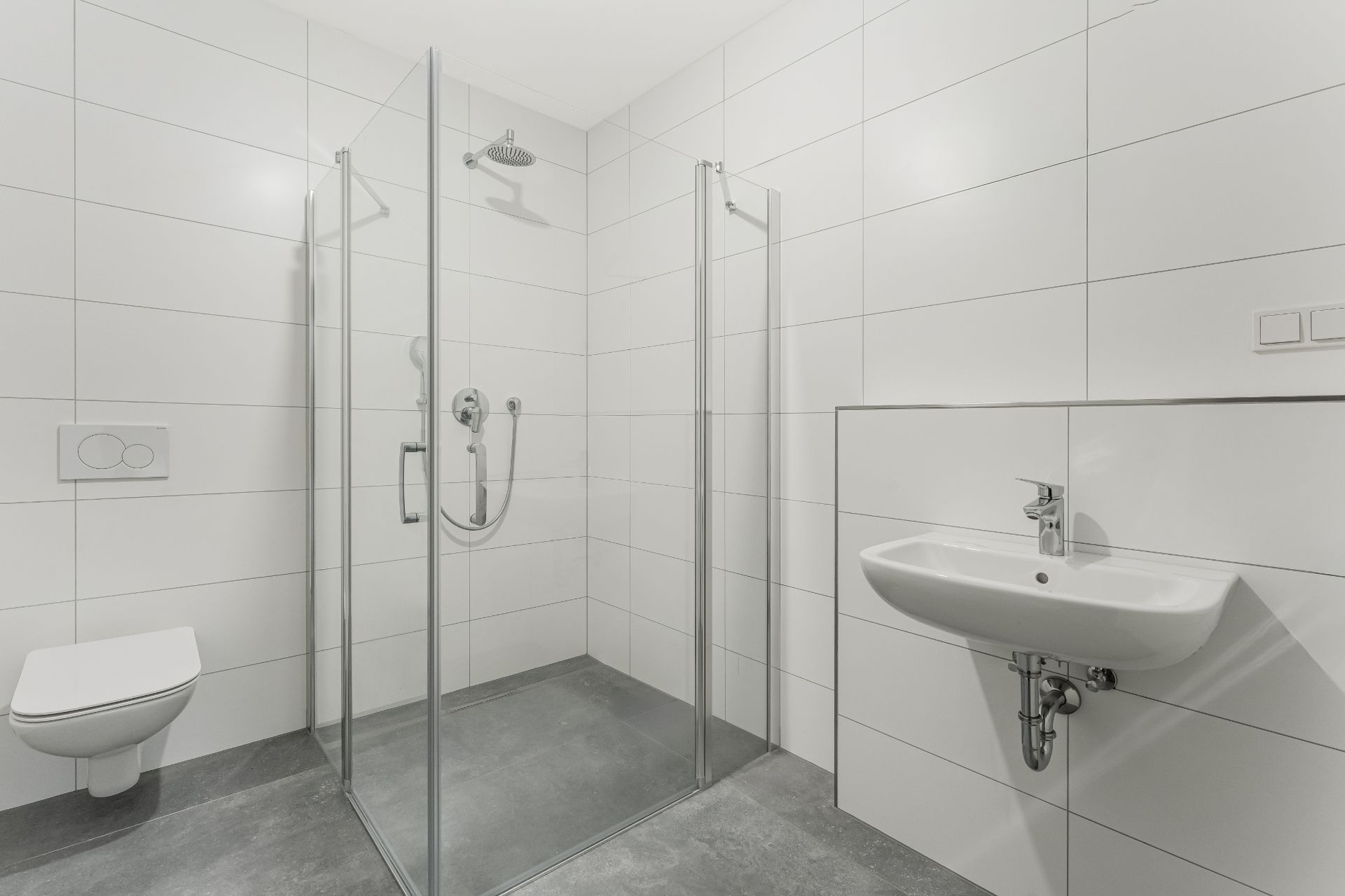 Modernes Badezimmer mit Glasdusche, Hänge-WC und Wandwaschbecken auf grauem Boden.