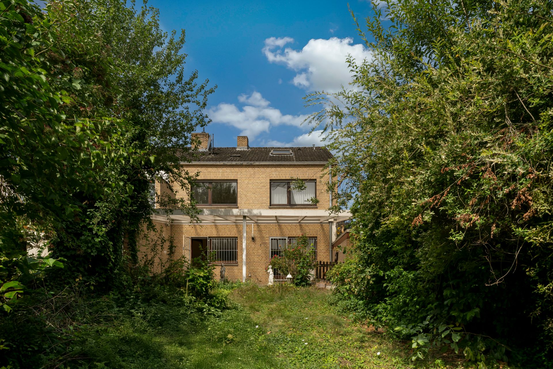 Rückseite eines zweistöckigen Hauses mit Garten und viel Bewuchs an den Seiten.