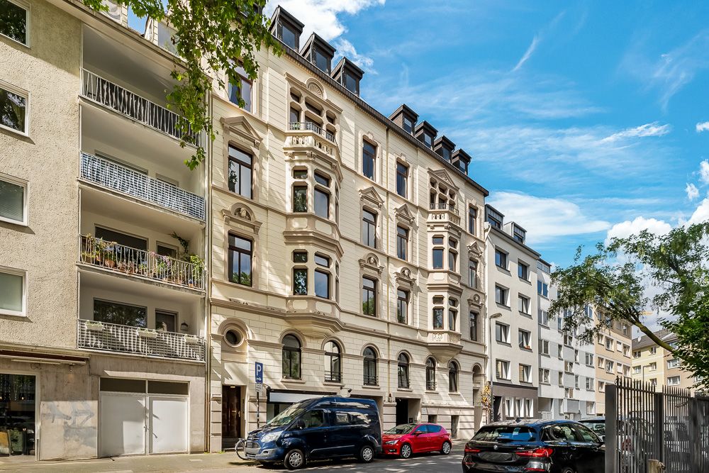 Mehrstöckiges Wohnhaus mit Verzierungen, geparkte Autos davor, blauer Himmel.