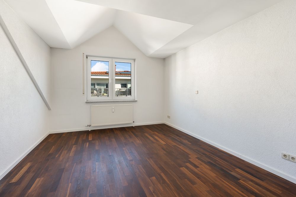 Leeres Zimmer mit weiß gestrichenen Wänden, Holzfußboden und Fenster mit Blick nach draußen.