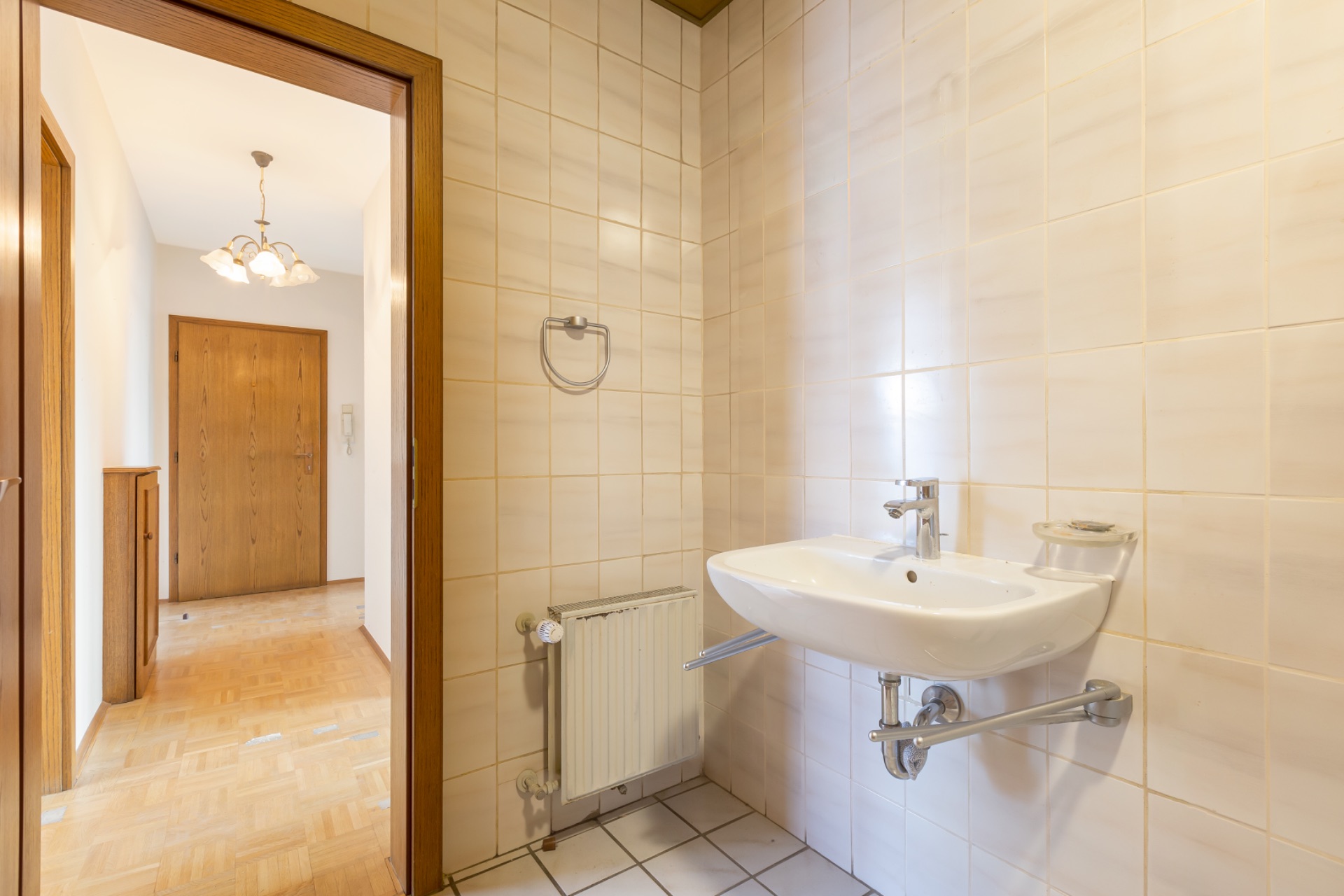 Badezimmer mit Waschbecken, Handtuchhalter und Blick auf einen Flur mit Holztür.