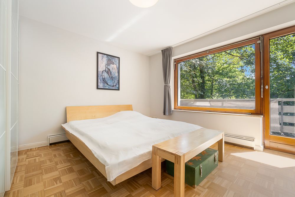 Helles Schlafzimmer mit Doppelbett, großem Fenster, Holzboden und Tisch am Bett.