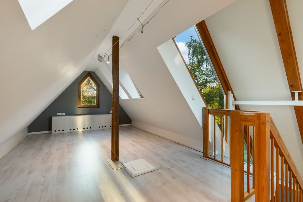Heller Dachbodenraum mit weißem Boden, Holzstütze, Fenster und Treppe mit Holzgeländer.
