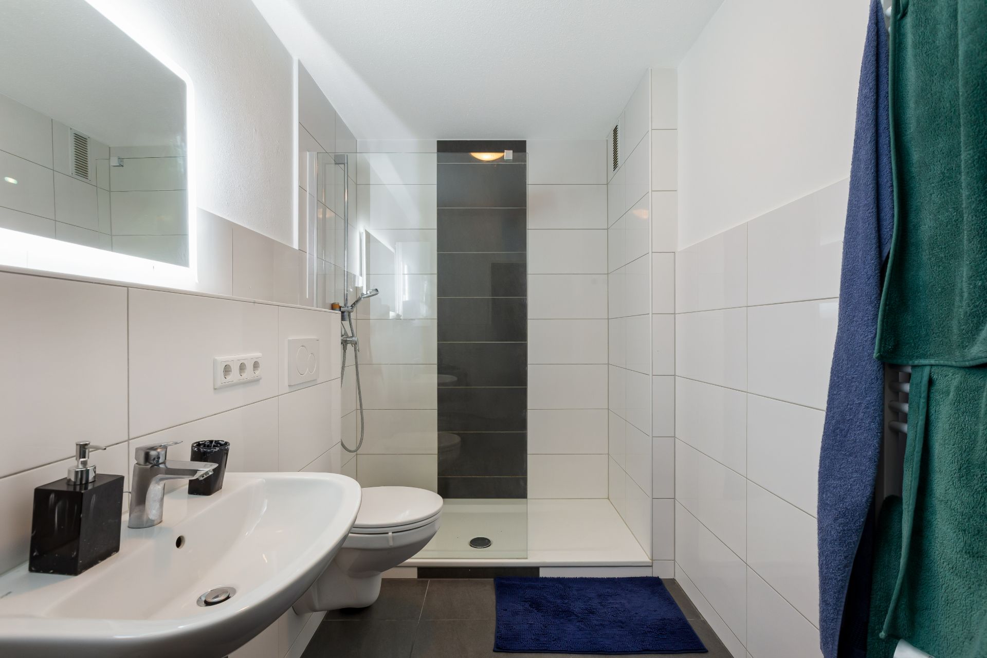 Modernes Badezimmer mit Dusche, Toilette, Waschbecken und beleuchtetem Spiegel.