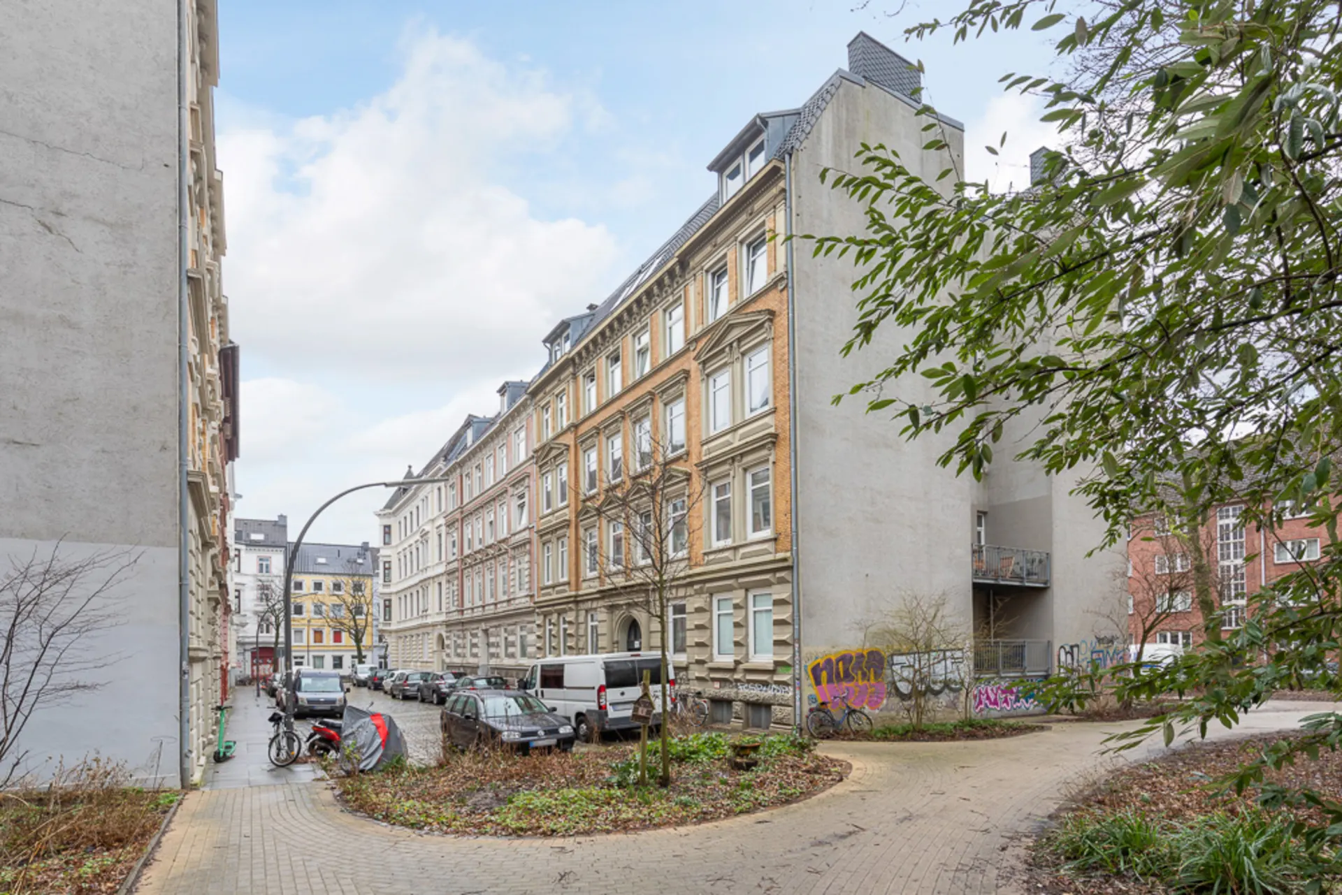 Wohngebäude an einer Kurve mit Autos, Fahrrädern und Graffiti an der Hauswand.