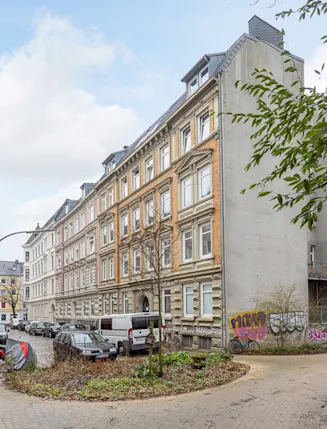 Wohngebäude an einer Kurve mit Autos, Fahrrädern und Graffiti an der Hauswand.