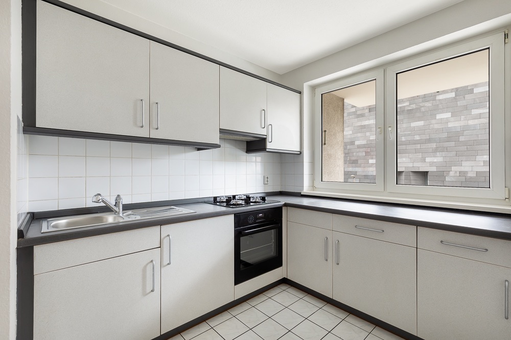 Moderne Einbauküche mit weißen Schränken, Gasherd, Backofen, Spüle und großem Fenster.