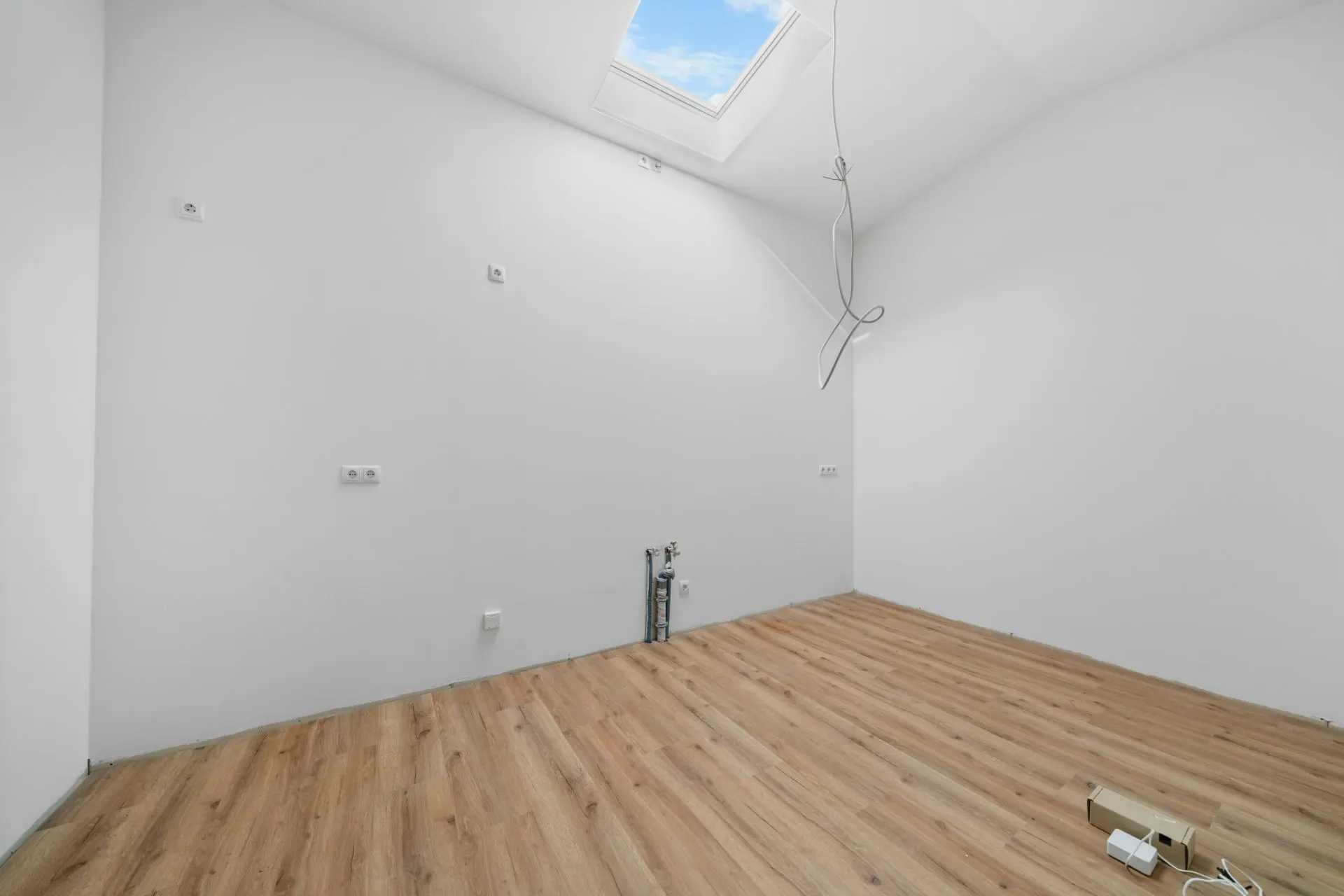 Leerer Raum mit weiß gestrichenen Wänden, Holzfußboden und Dachfenster.