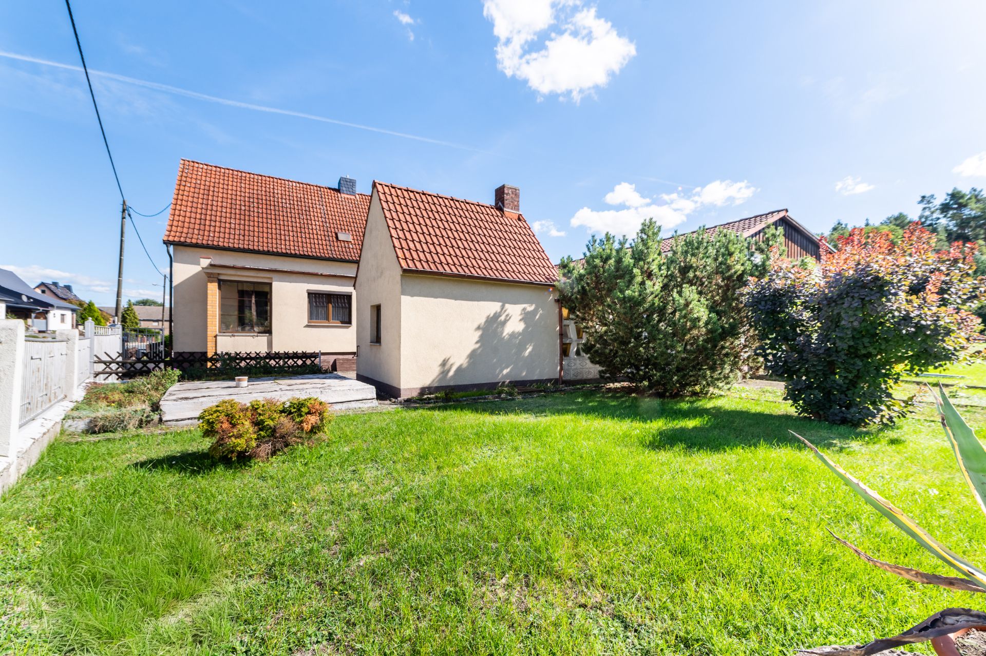 Einfamilienhaus mit rotem Dach und großem Garten, Bäume und Sträucher im Vordergrund.