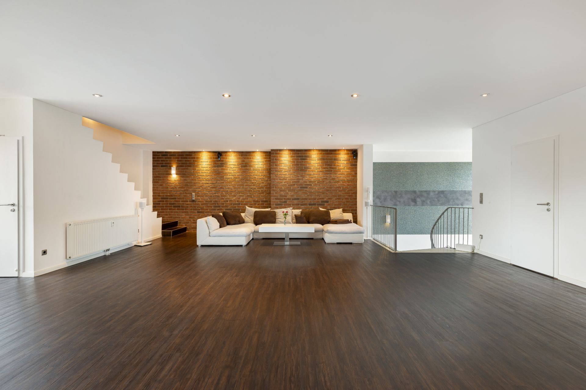 Großes Wohnzimmer mit dunklem Holzboden, weißem Sofa und Backsteinwand.