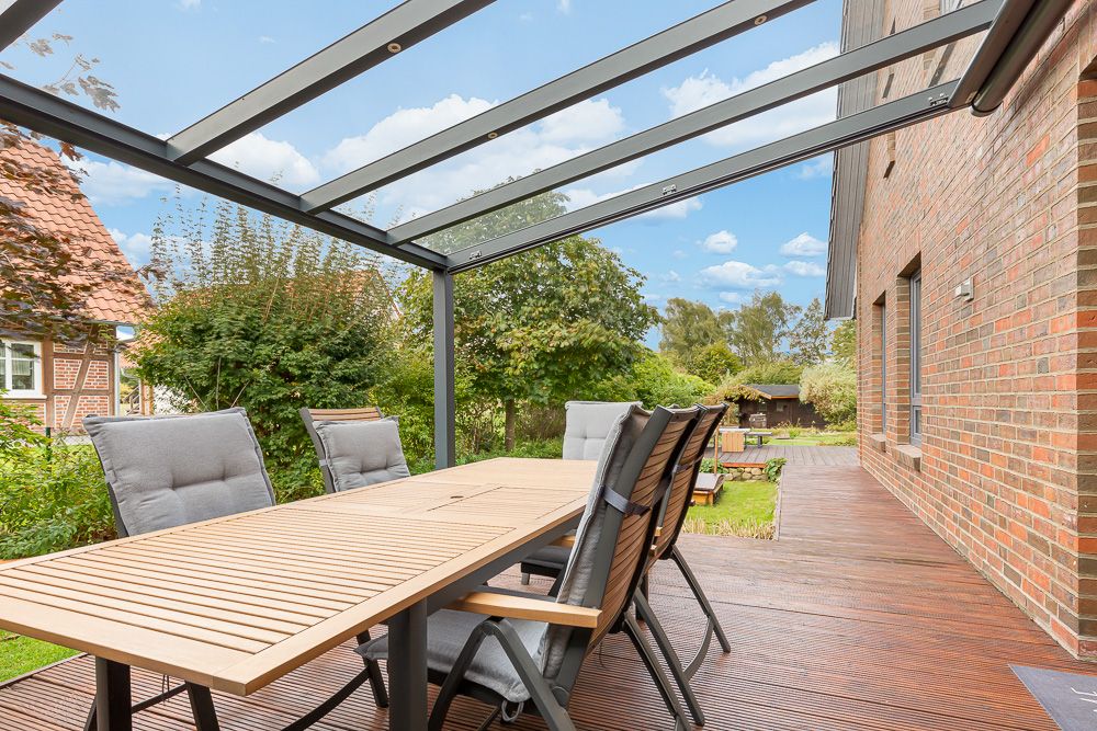 Überdachte Terrasse mit Holztisch, sechs Stühlen und Blick in einen grünen Garten.