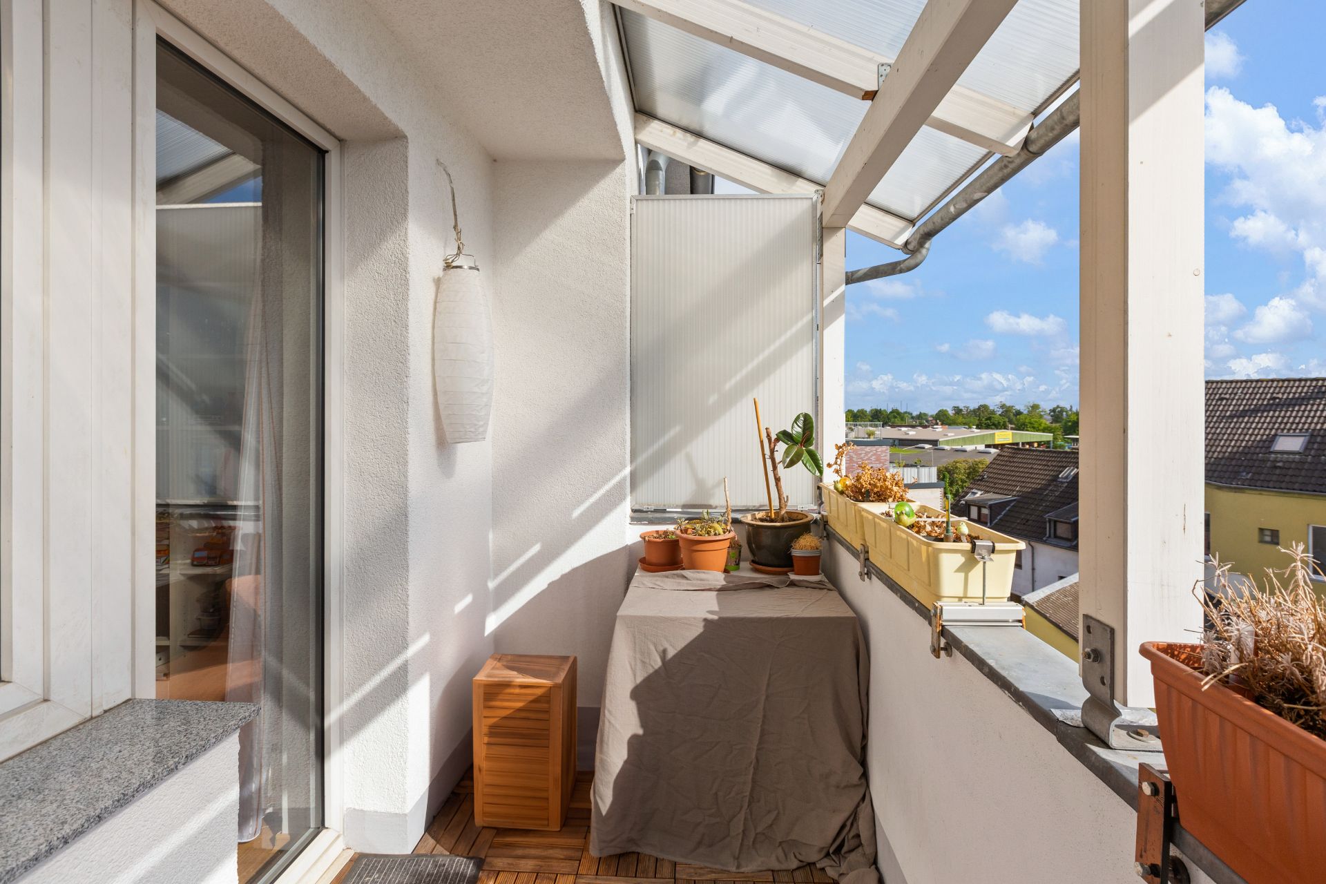 Überdachter Balkon mit Blumentöpfen, Blumenkasten und Blick auf Nachbarhäuser.