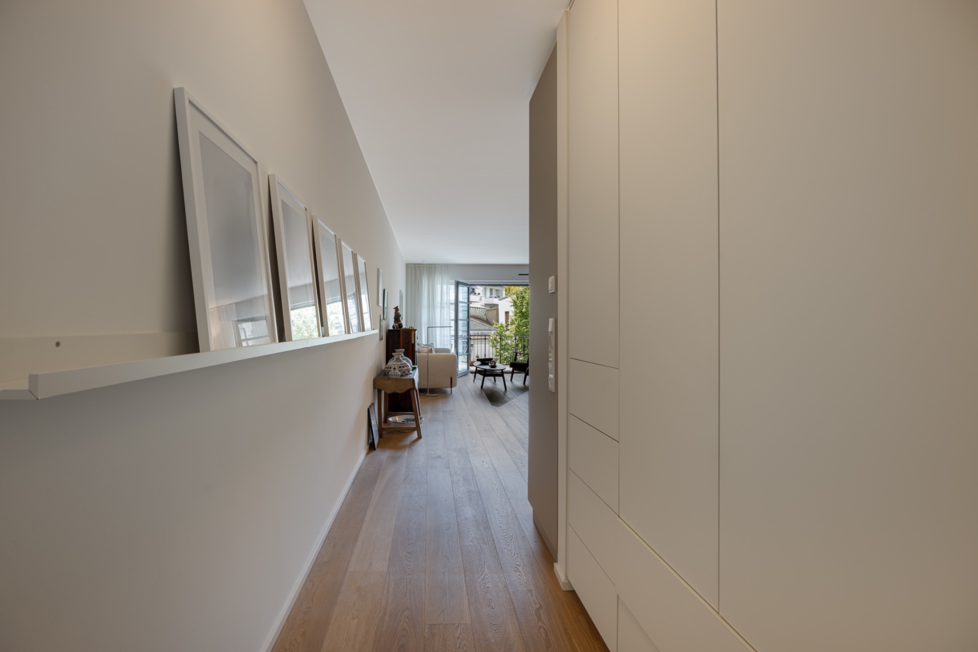 Heller Flur mit Holzboden, Bildern an der Wand und Blick ins Wohnzimmer.