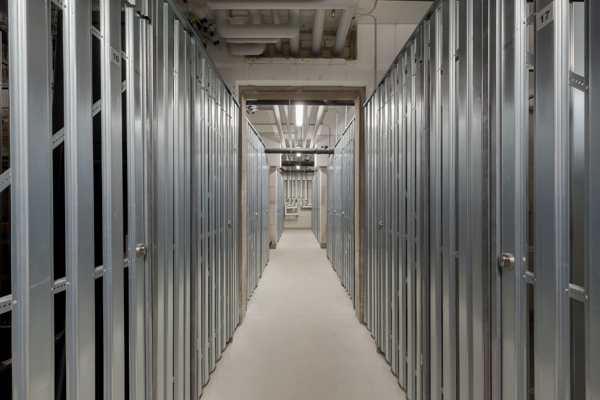 Gang mit Metallabteilen und sichtbaren Rohren an der Decke.