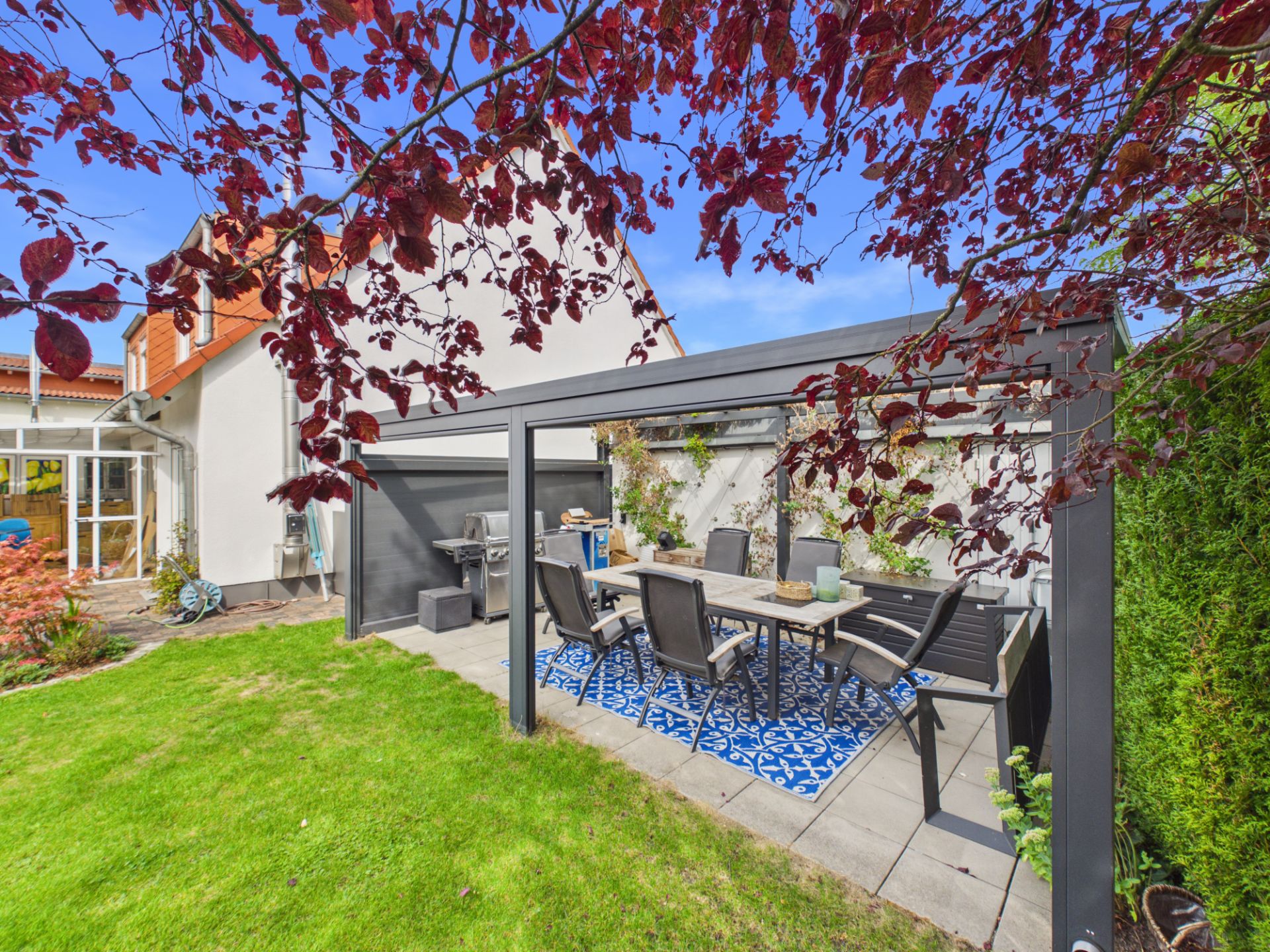 Überdachte Terrasse mit Esstisch und Stühlen im Garten eines Wohnhauses.
