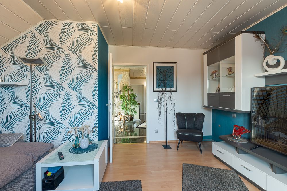 Wohnzimmer mit gemusterter Tapete, Sofa, Teppichen und Regalwand mit Fernseher.