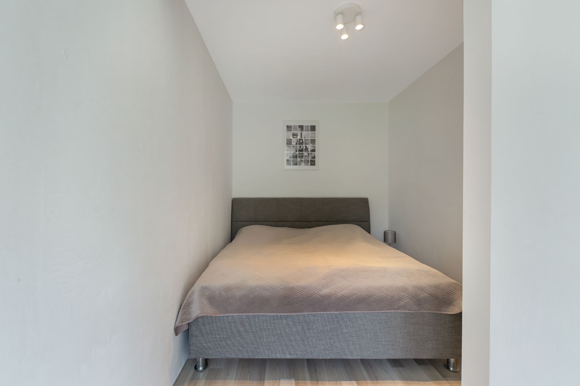 Kleines Schlafzimmer mit einem Doppelbett, Bild an der Wand und Nachttischlampe.