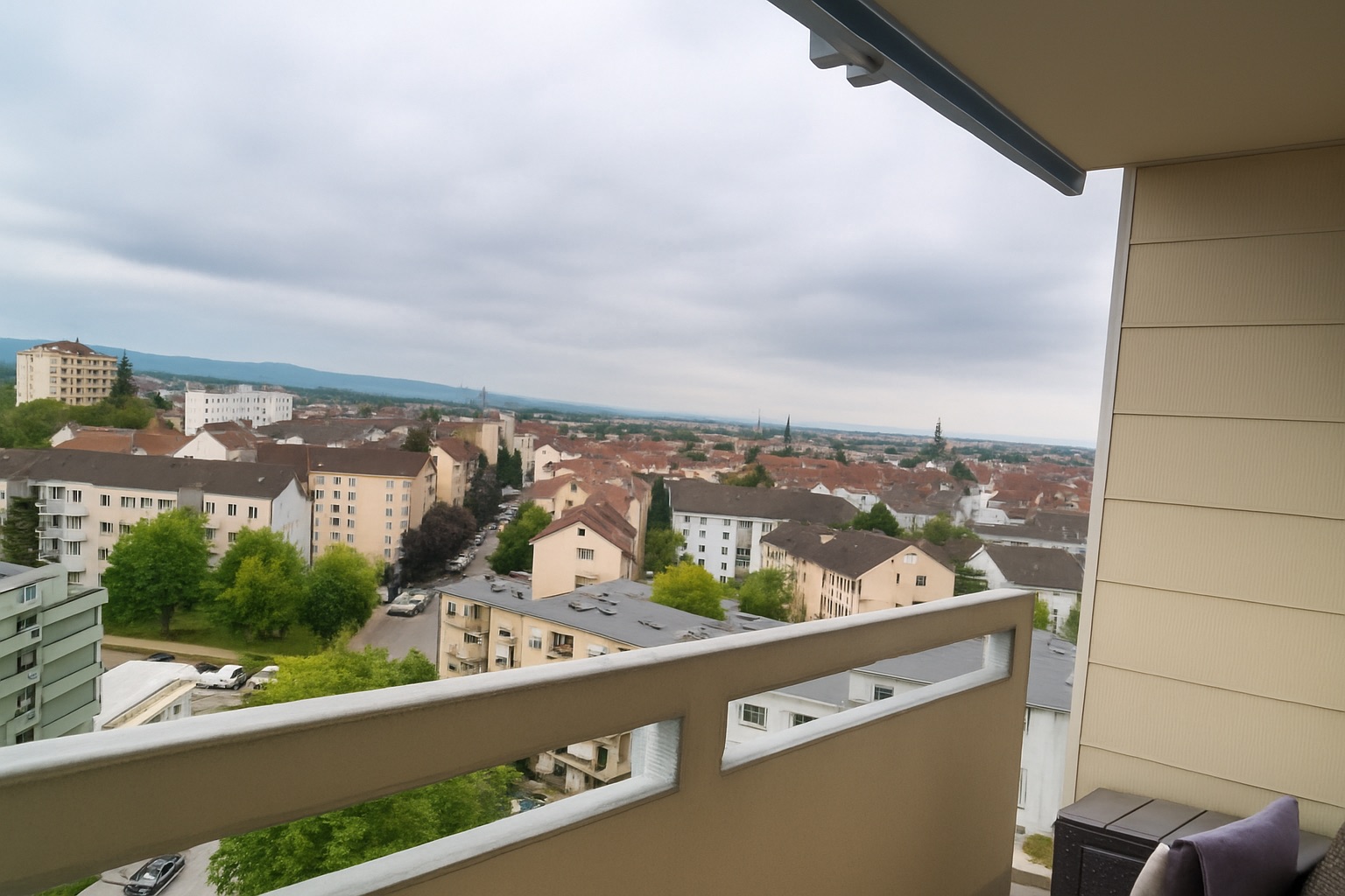 Blick von einem Balkon auf Wohnhäuser und eine Stadtlandschaft bei bewölktem Himmel.