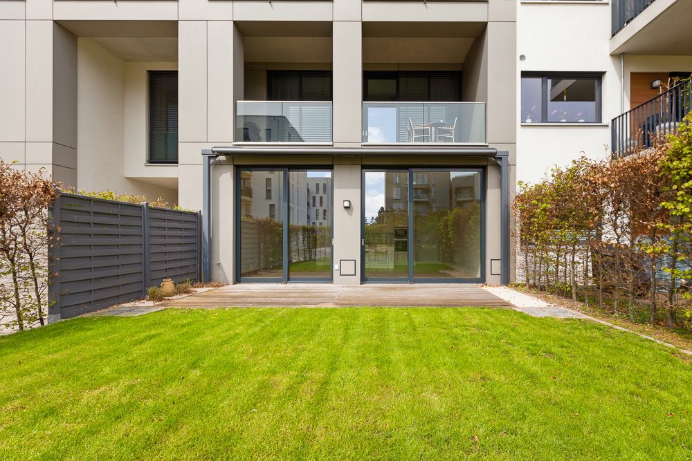 Moderne Wohnhaus-Terrasse mit Rasenfläche, Glastüren und Balkon darüber.