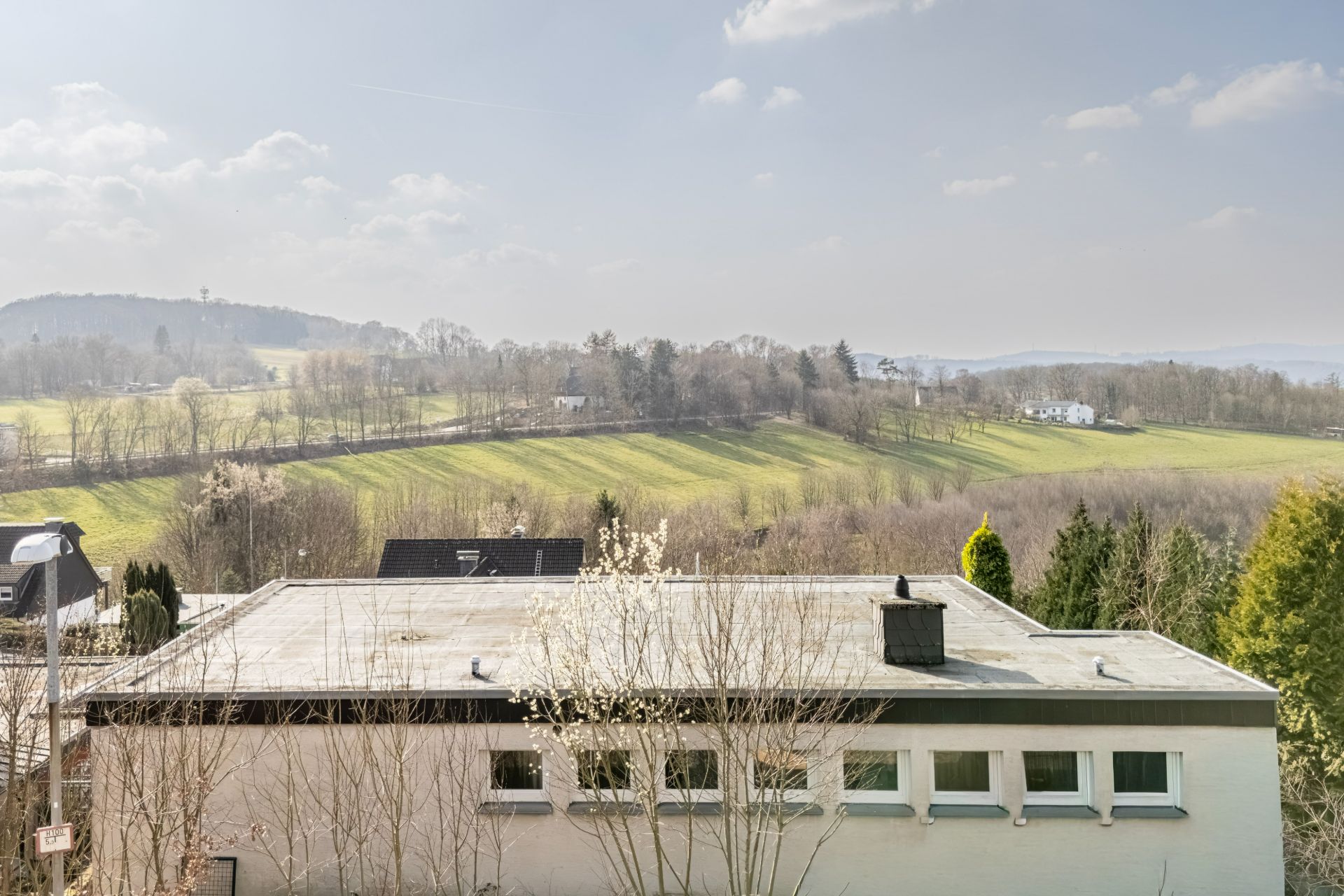 Flachdachhaus im Vordergrund mit Blick auf Wiesen, Bäume und Hügel im Hintergrund.
