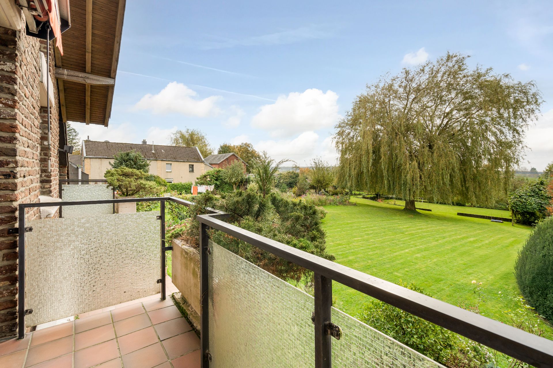 Blick von einem Balkon auf einen großen Garten mit Rasenfläche und einem großen Baum.