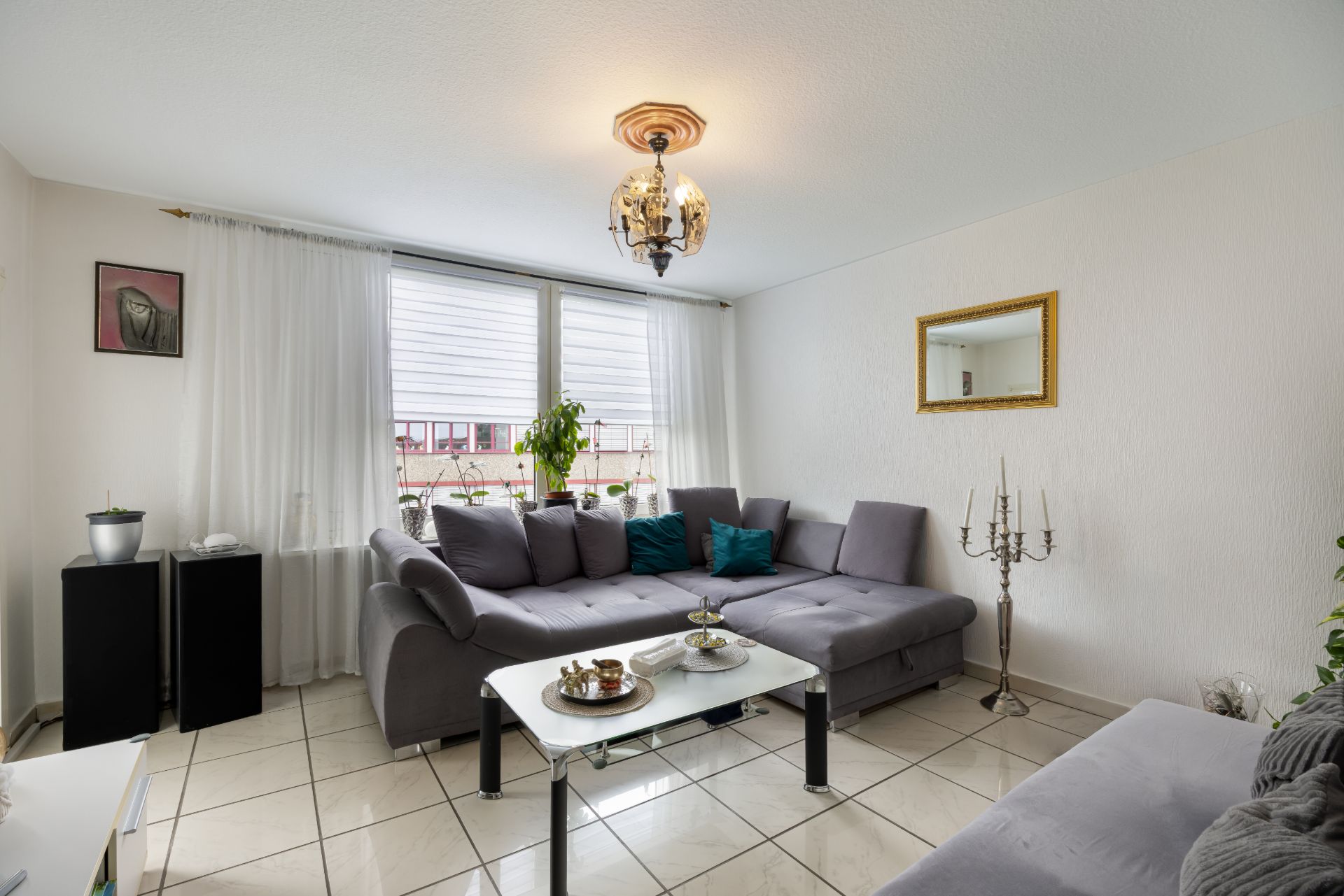 Helles Wohnzimmer mit Ecksofa, Couchtisch und großem Fenster mit weißen Vorhängen.