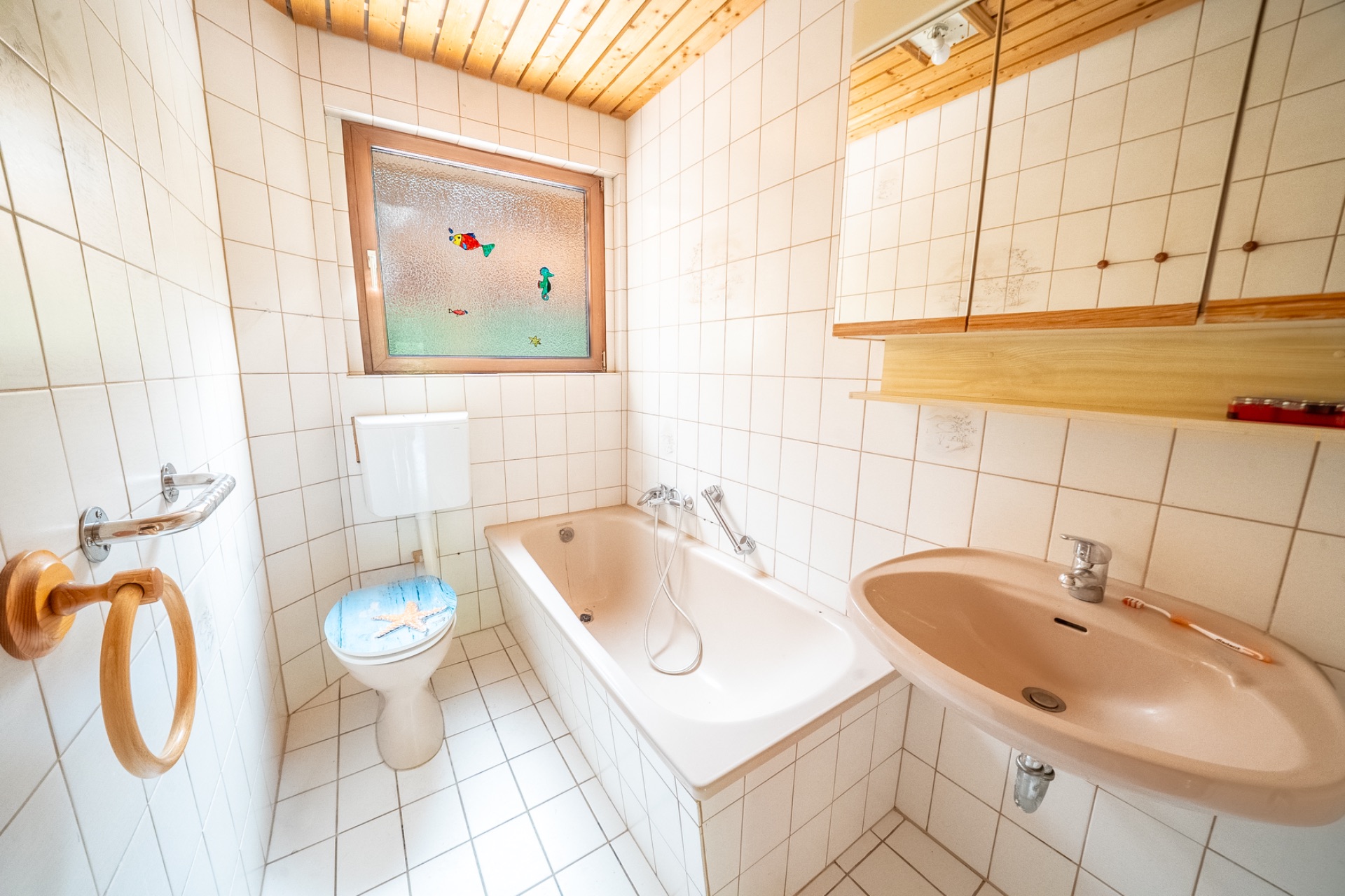 Helles Bad mit Badewanne, Toilette, Waschbecken und Fenster mit Milchglas.