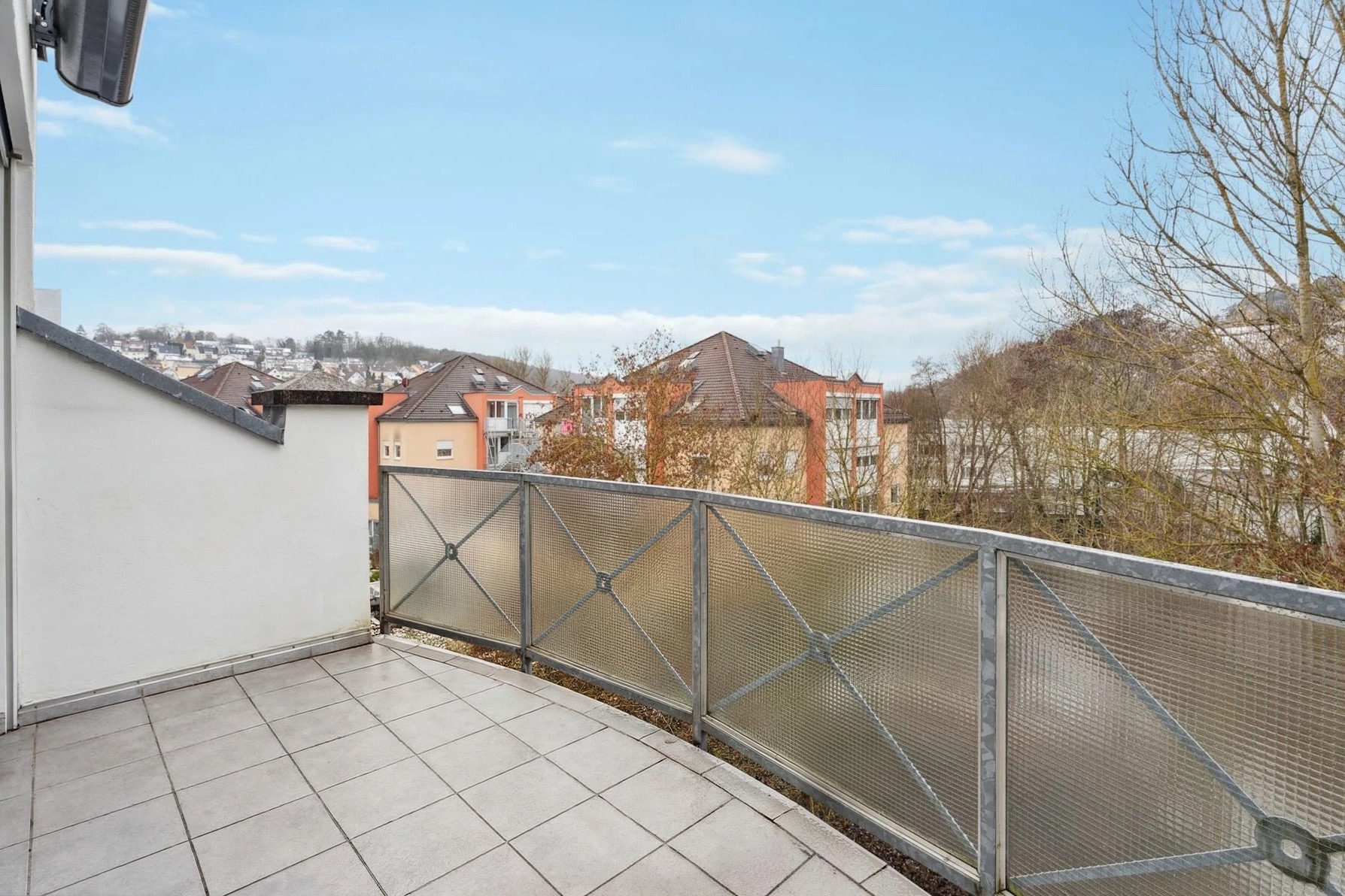Balkon mit Fliesenboden und Metallgeländer, Blick auf Wohngebäude und Bäume.