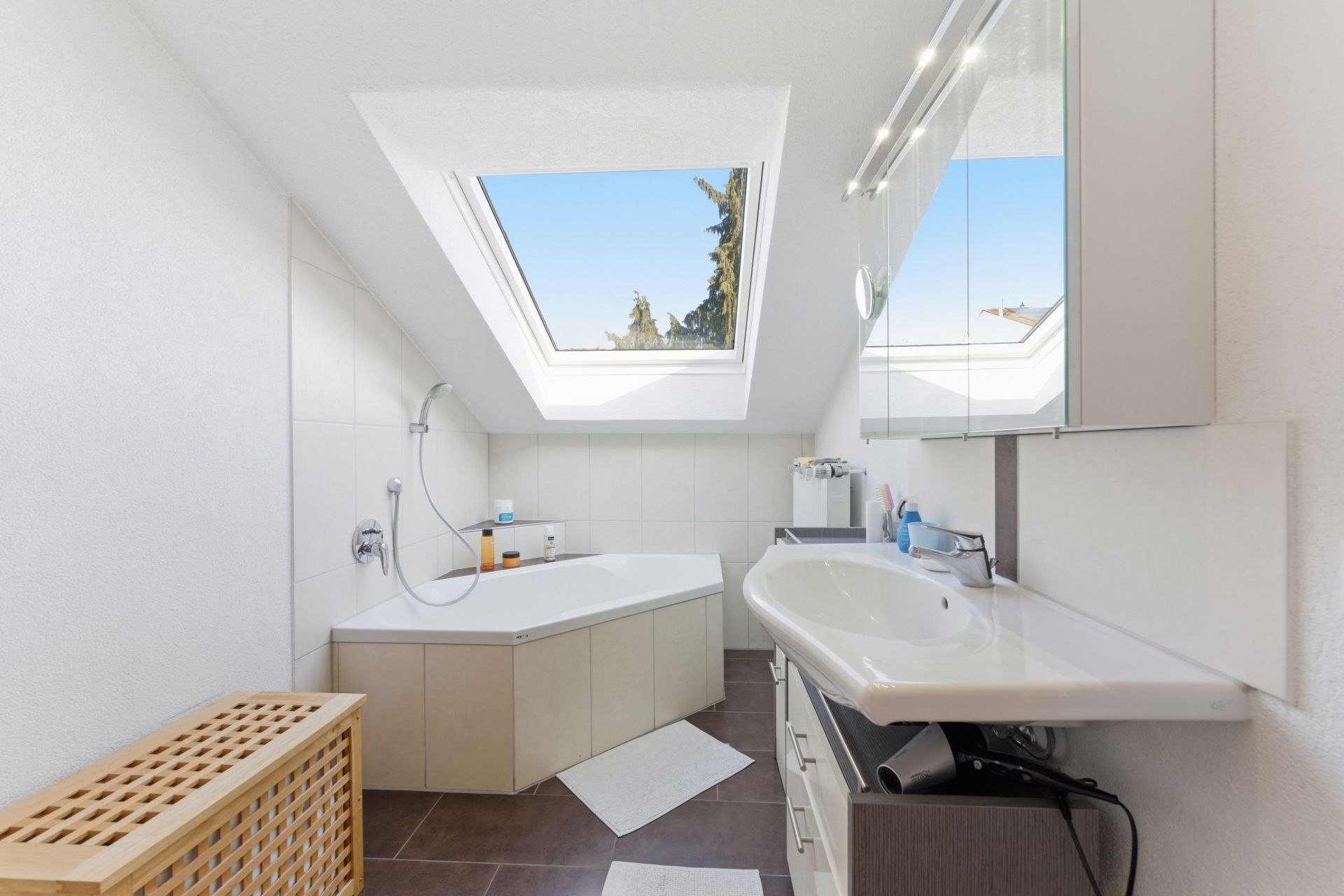 Helles Badezimmer mit Badewanne, Dachfenster und Waschbecken unter einer Schräge.