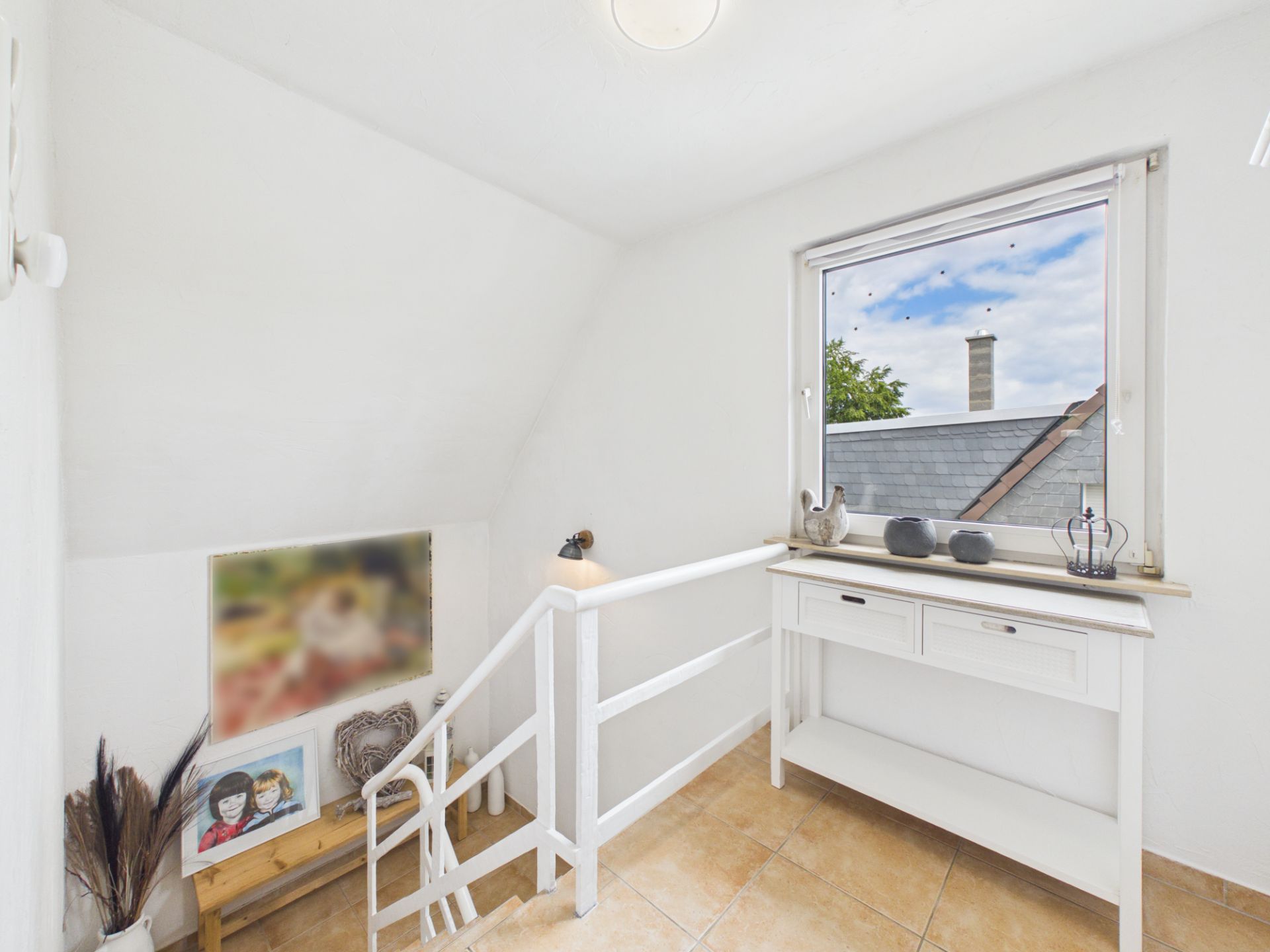 Heller Flur mit Fenster, weißem Tisch, Dekoration und Treppe, Fliesenboden.