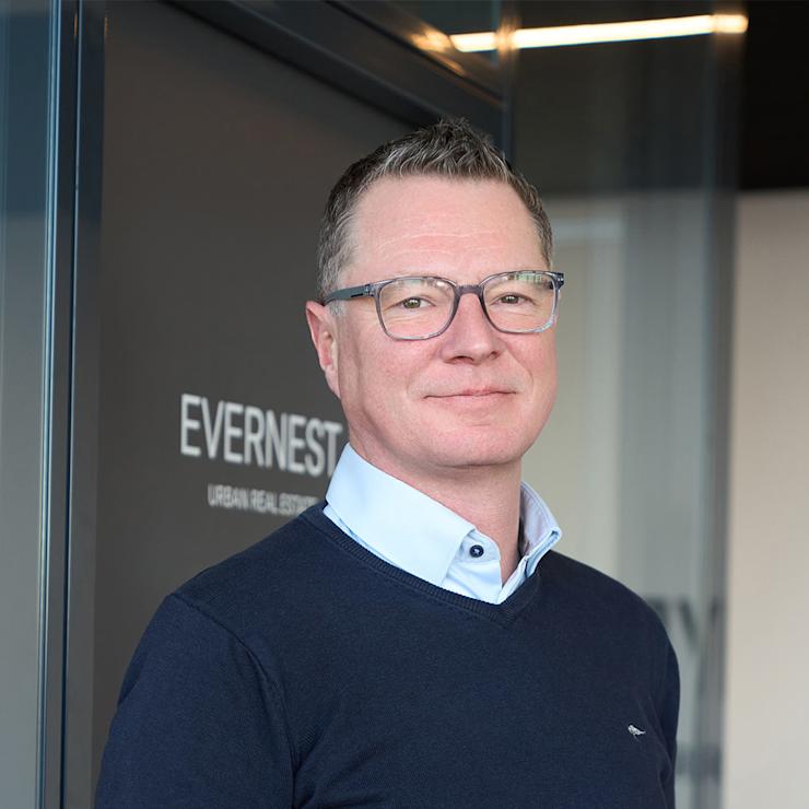 Ein Mann mit Brille und blauem Pullover steht vor einer Glastür.