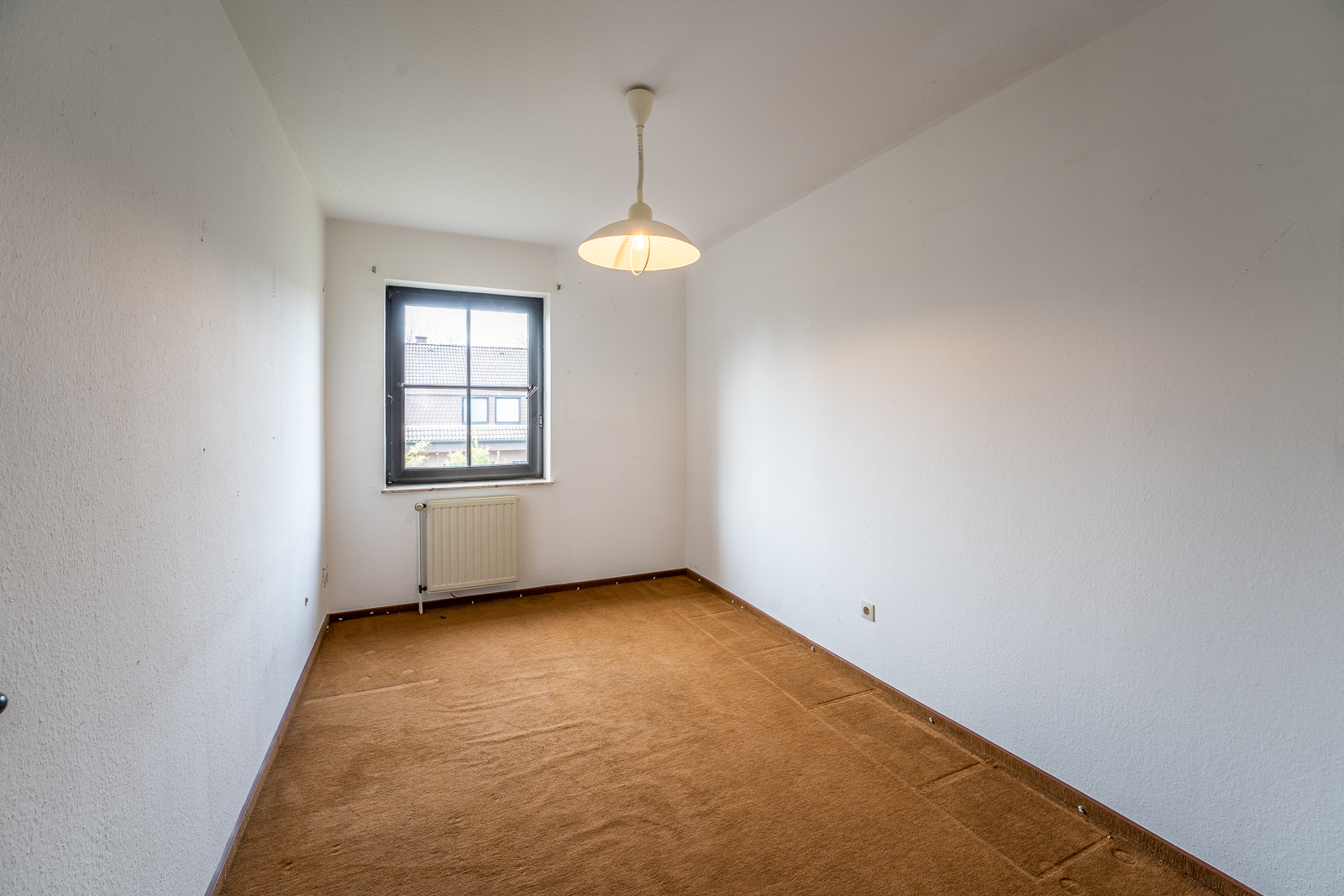 Leeres Zimmer mit braunem Teppich, weißer Wand, Fenster und Deckenlampe.