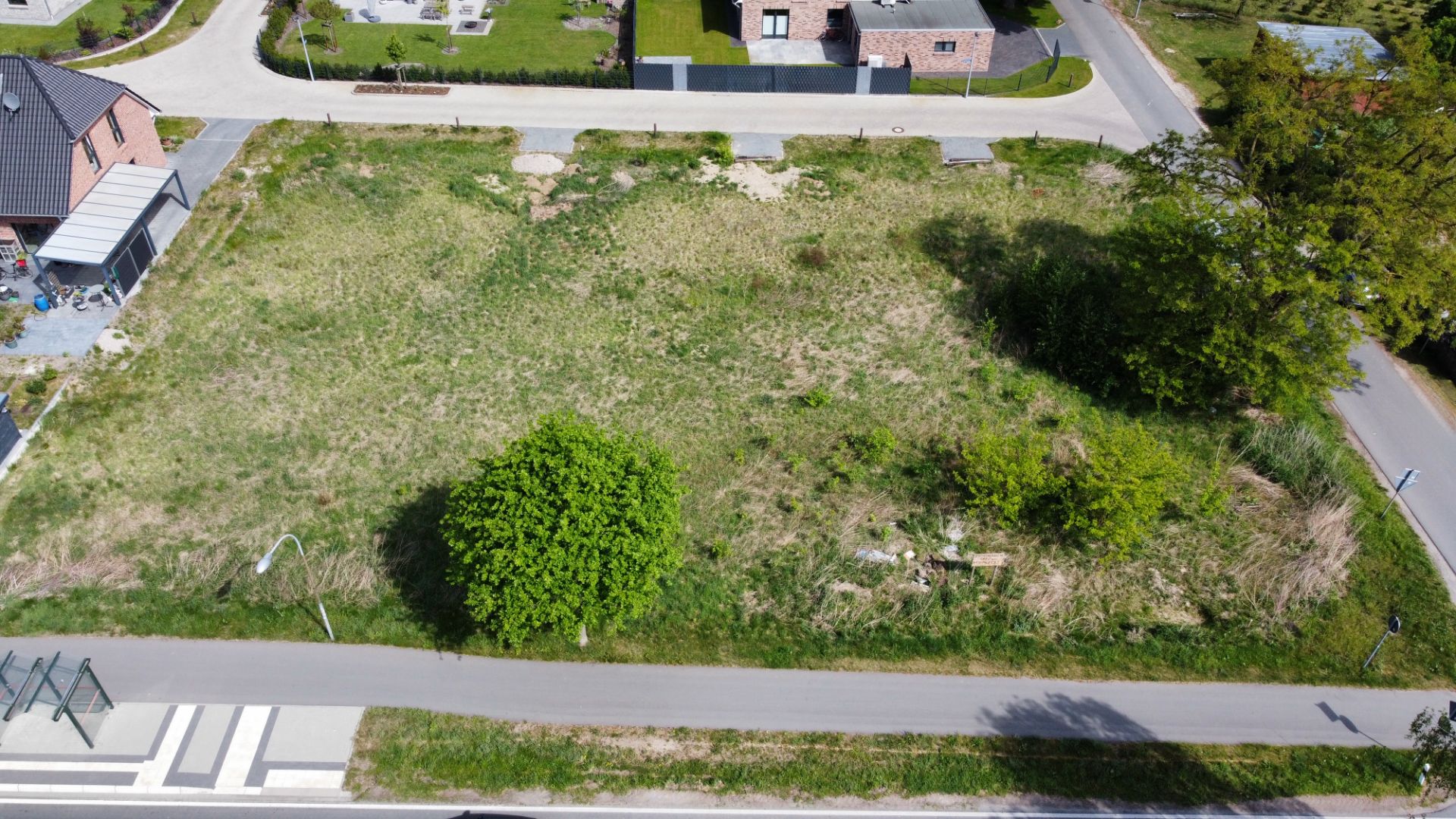 Luftaufnahme eines unbebauten Grundstücks mit Gras und einigen Büschen an einer Straßenecke.